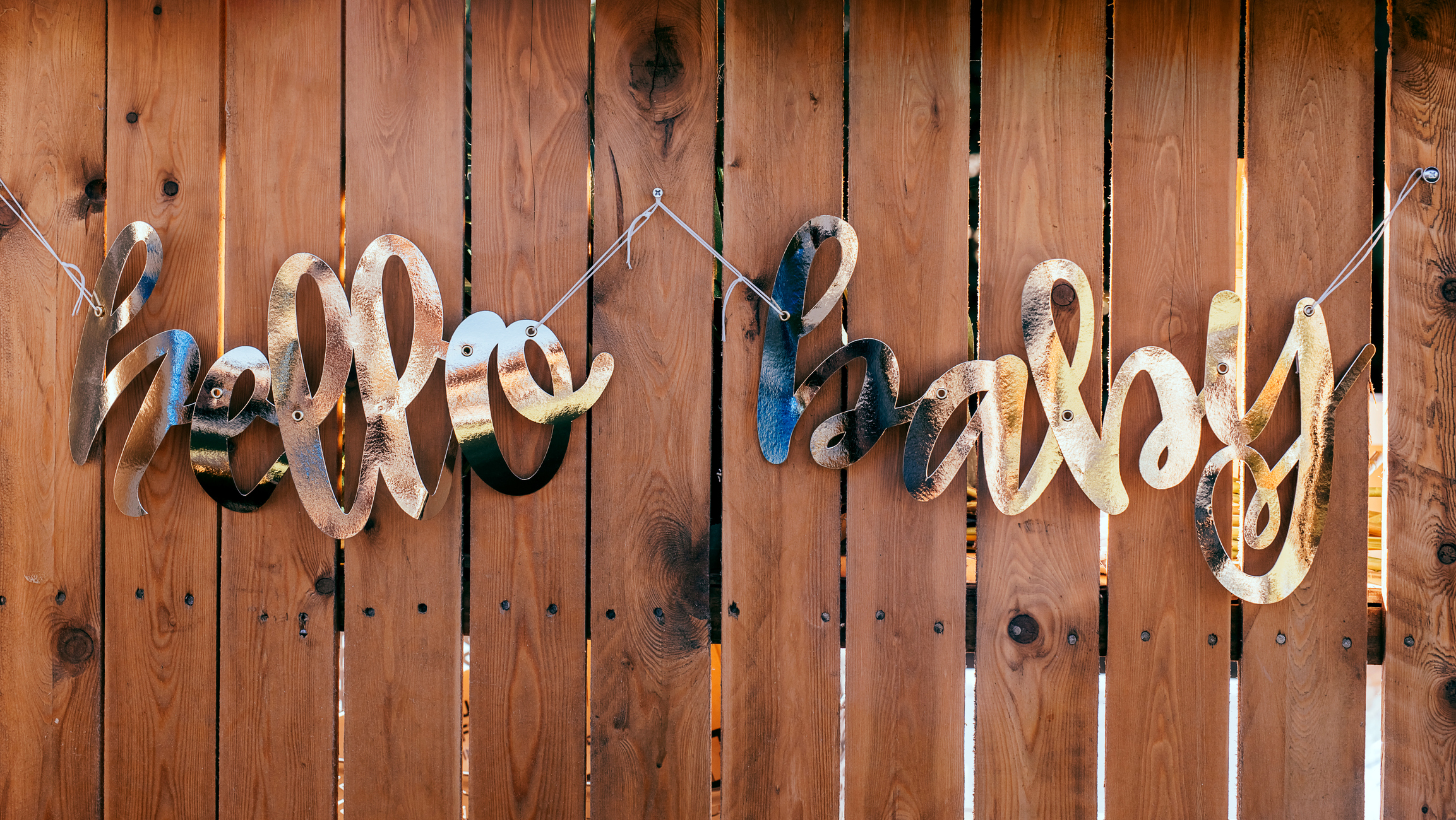 Words HELLO BABY made of golden foil on wooden background.