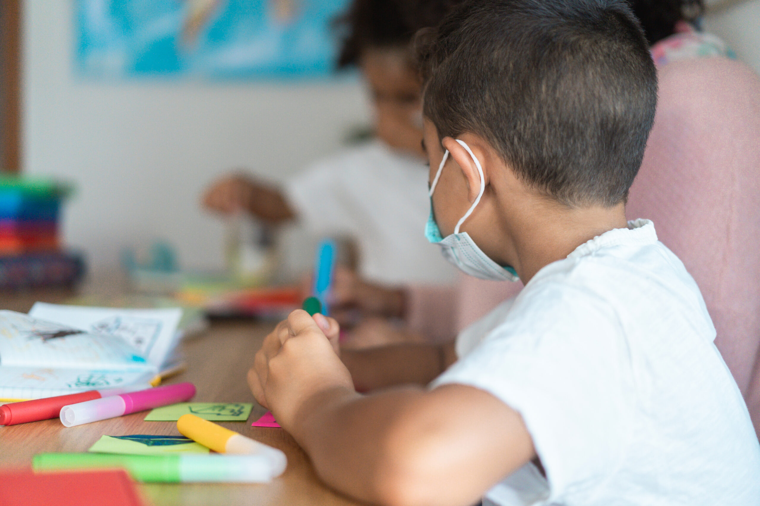 Boy painting in preschool classroom wearing face protective mask - Back to school during coronavirus outbreak concept - Focus on kid's ear