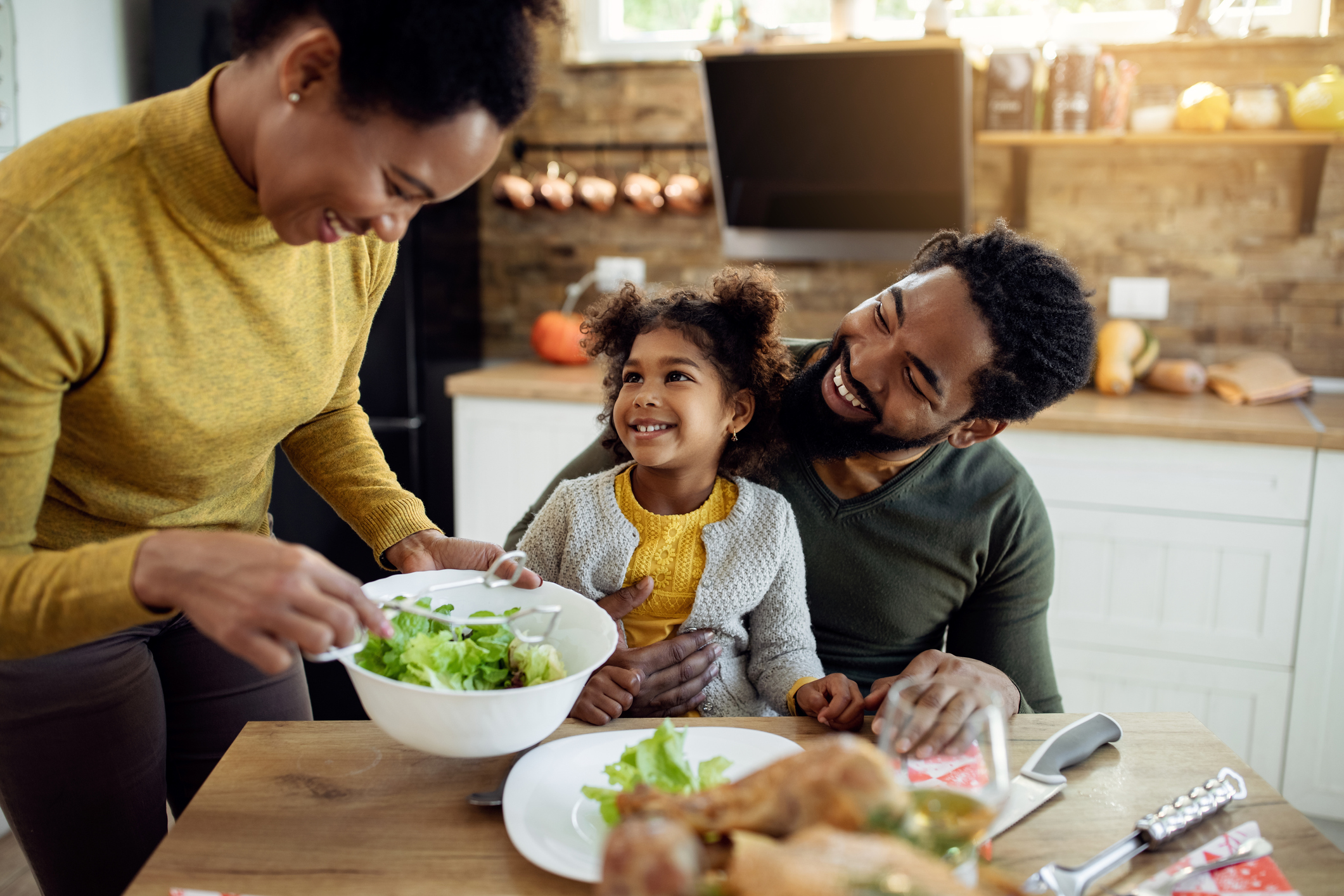 Happy African American girl having Thanksgiving lunch with her parents at dining table.