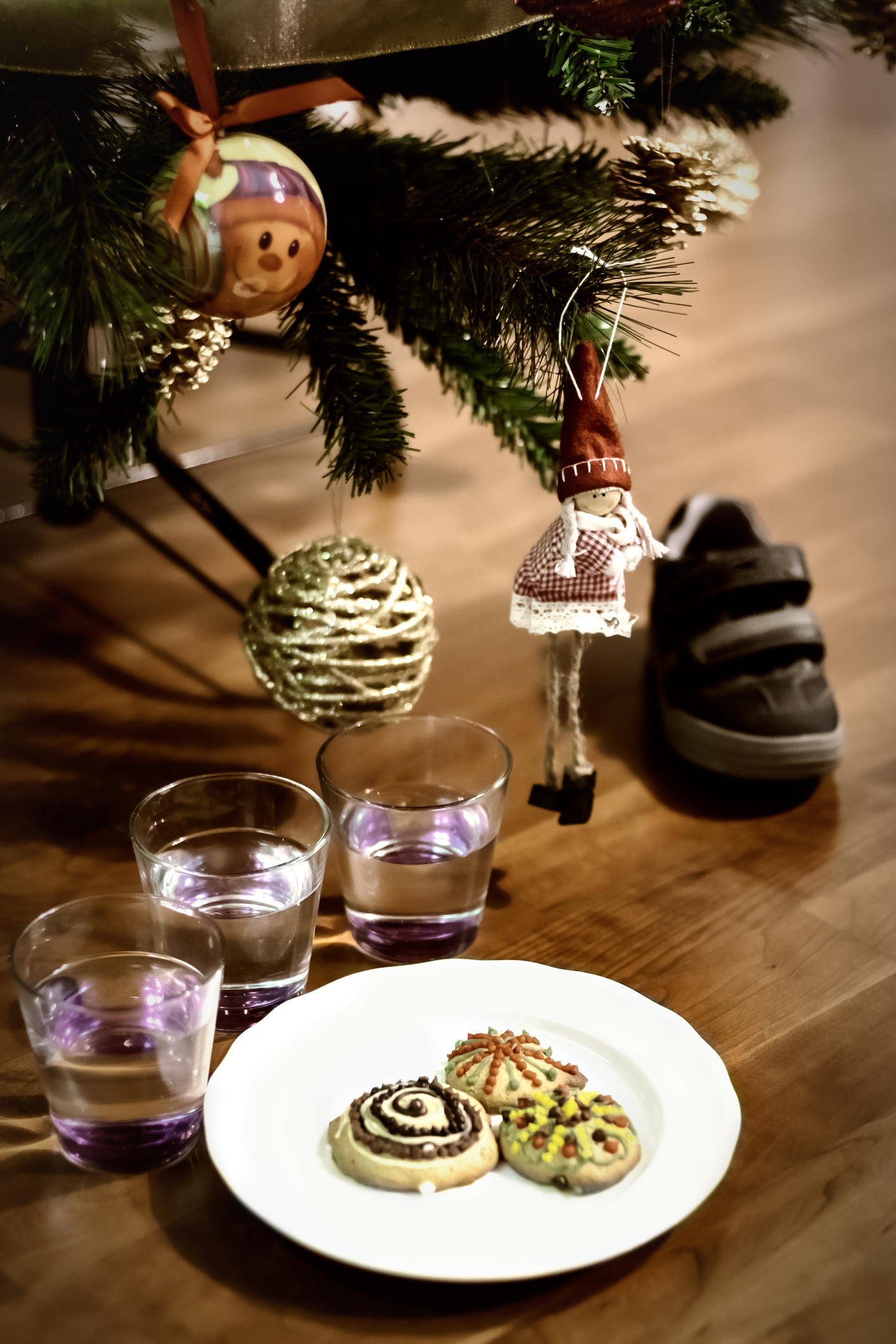 Three decorated cookies and three glasses of water at the feet of a Christmas tree with a shoe waiting for the gifts on the night of the three kings night