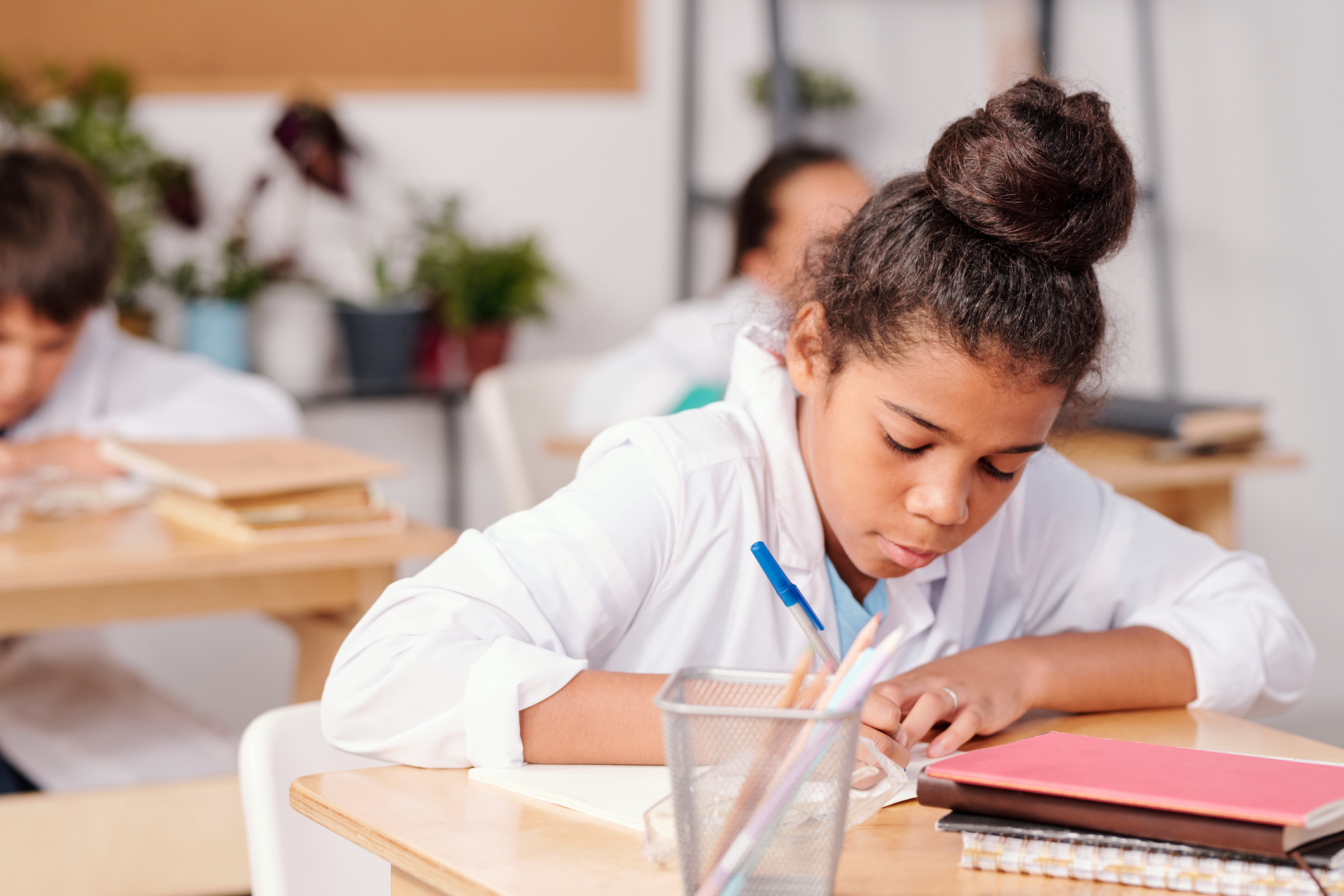 Contemporary mixed-race schoolgirl in whitecoat writing down chemical formula