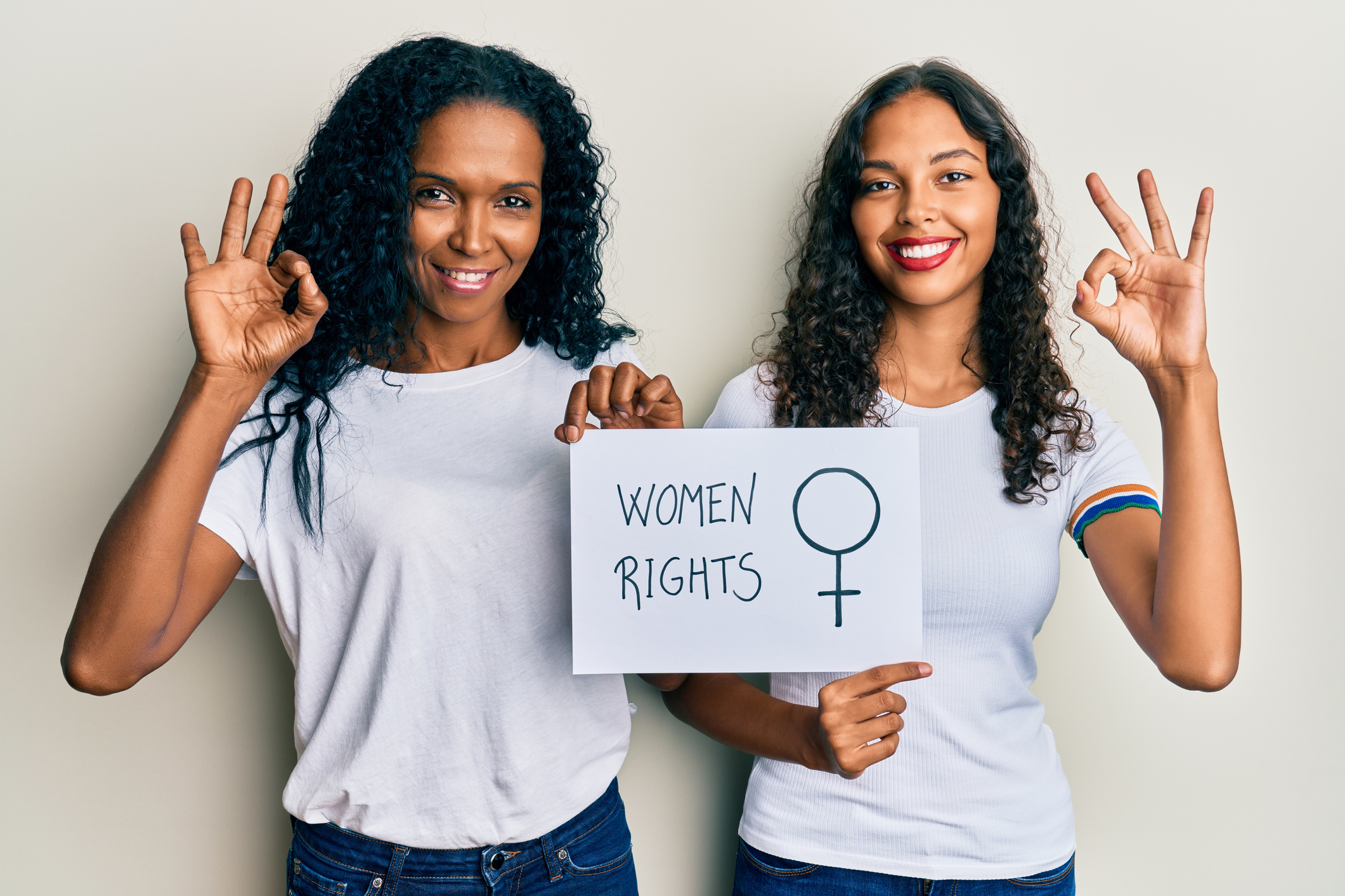 African american mother and daughter holding women rights banner doing ok sign with fingers, smiling friendly gesturing excellent symbol