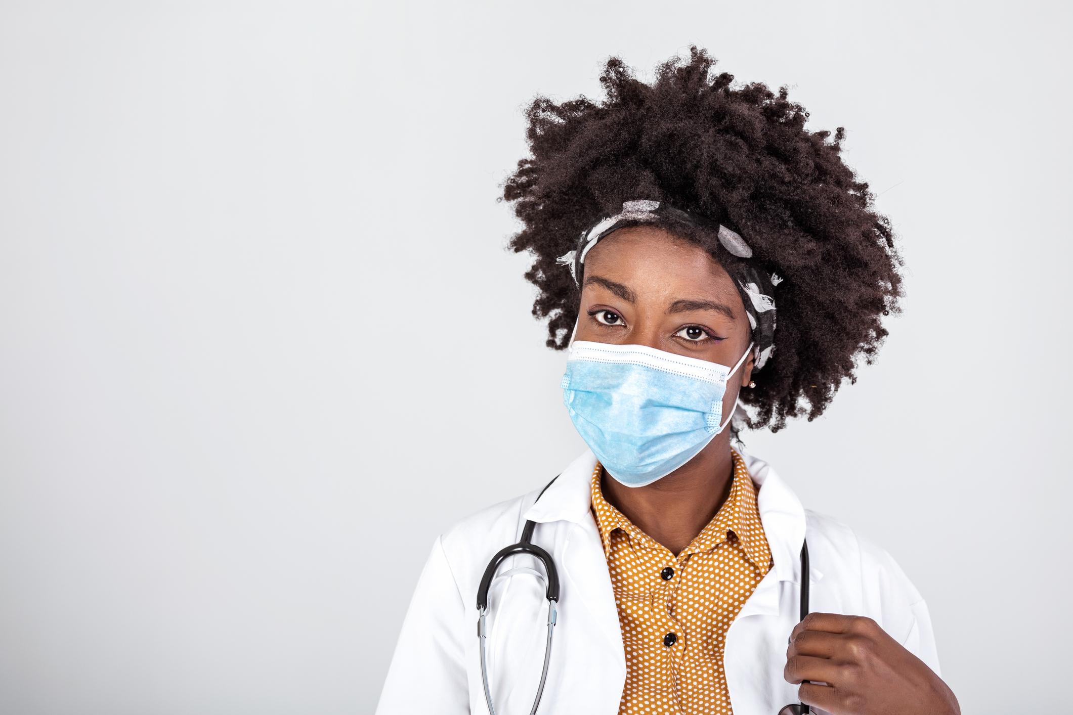 Portrait of young beautiful black female EMS medical worker,wearing uniform and protective face mask,studio headshot isolated on white background,stress and worry due to Coronavirus COVID-19 pandemic