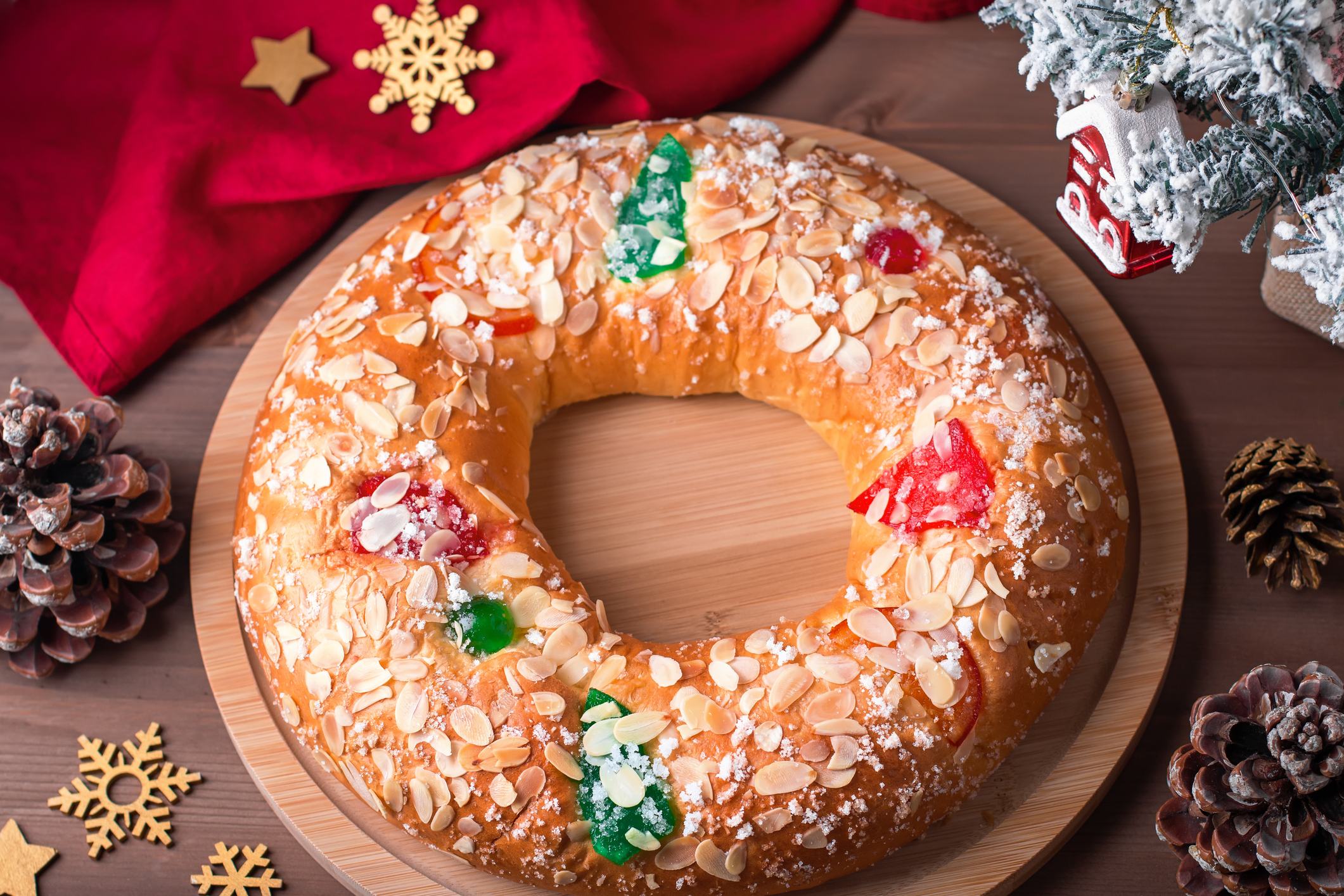 Traditional Epiphany cake Roscon de Reyes on wooden table top with small Christmas tree and decoration closeup, top view