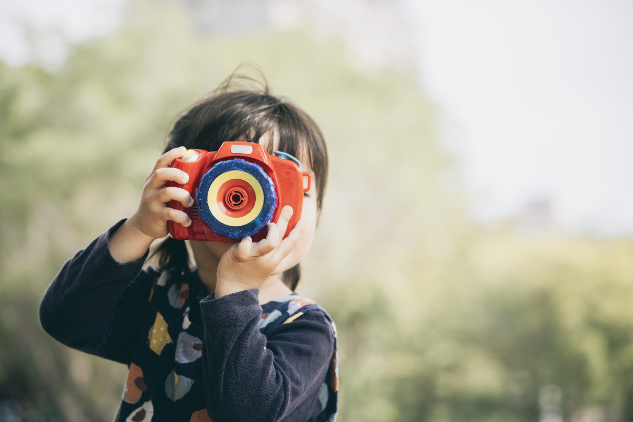 Asian little girl playing with toy camera in the park