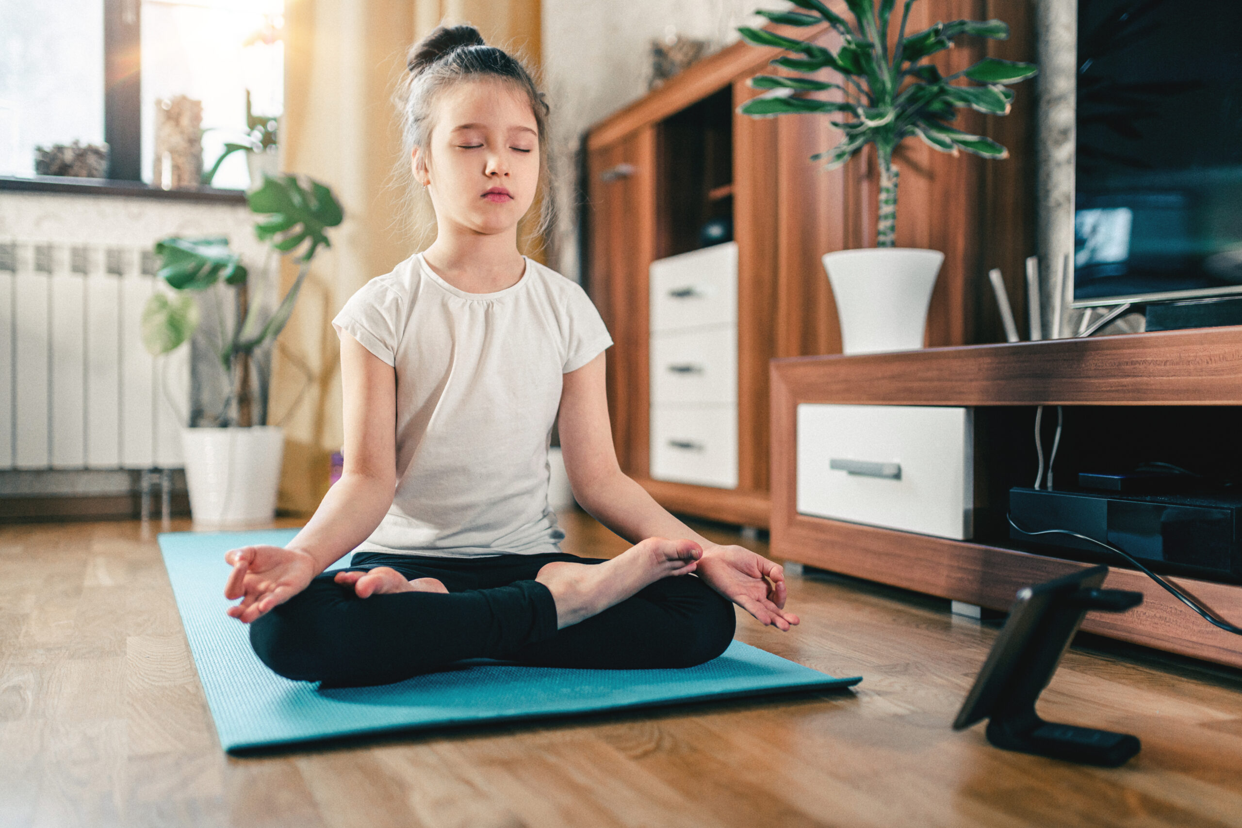 Yoga training online. Cute girl at home with digital tablet in lotus position