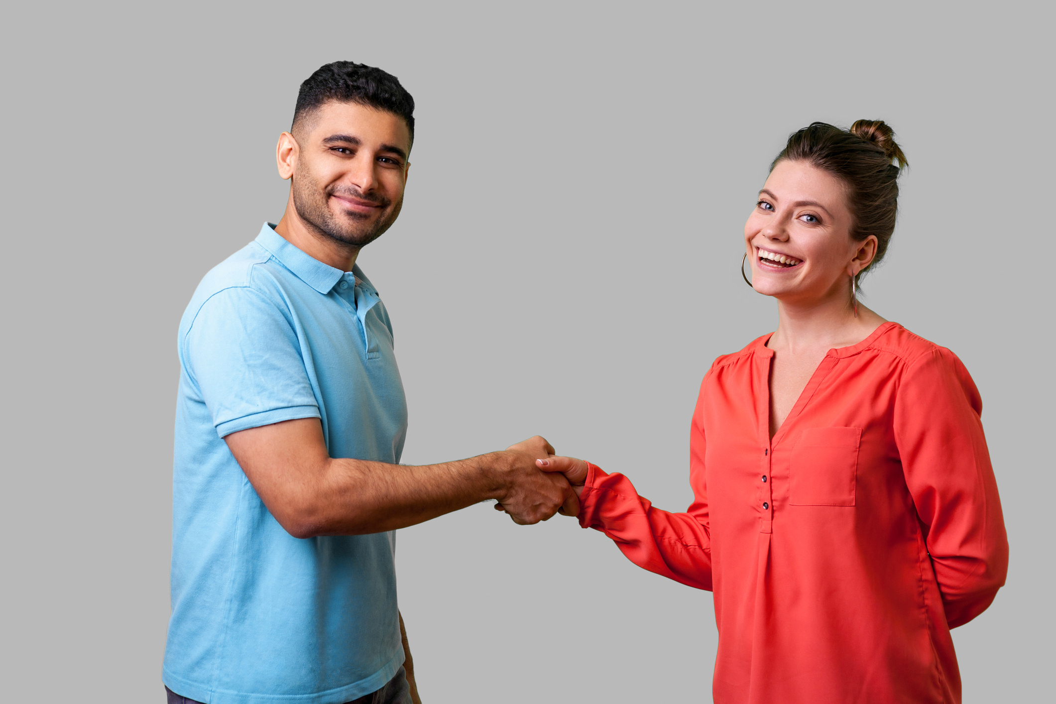 Portrait of lovely young couple in casual wear standing and shaking hands. isolated on gray background