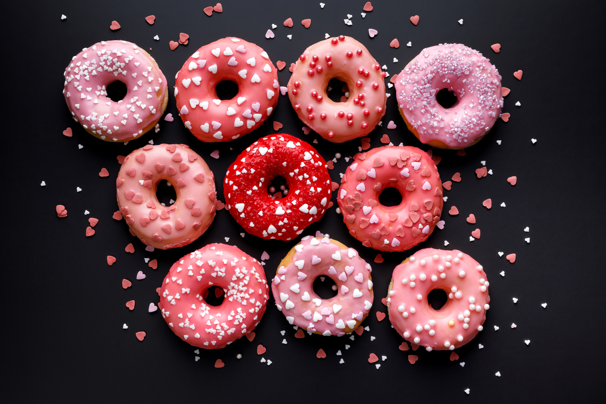 Valentine's donuts with sweet glaze and various sprinkles on a black background