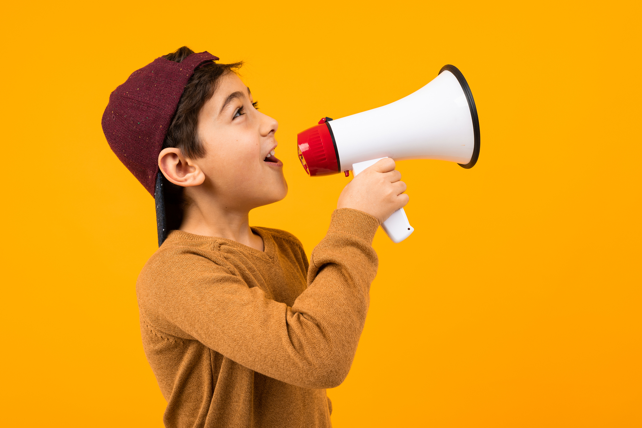 attractive european boy shouting news in a megaphone for a poster on an orange studio background