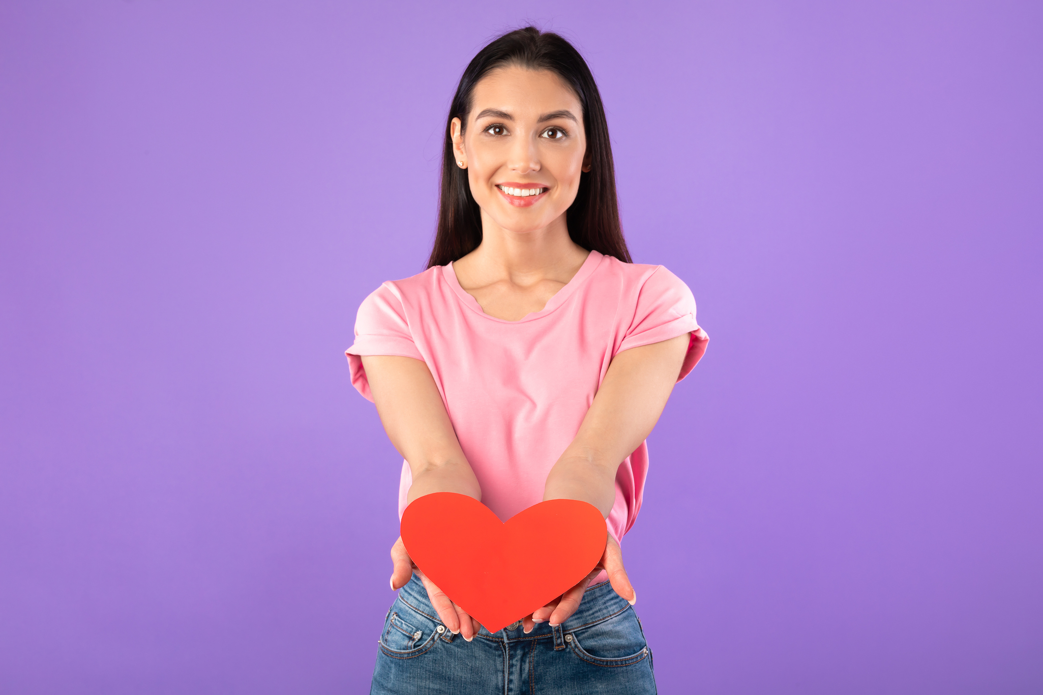 Smiling woman holding heart, showing it to camera camera