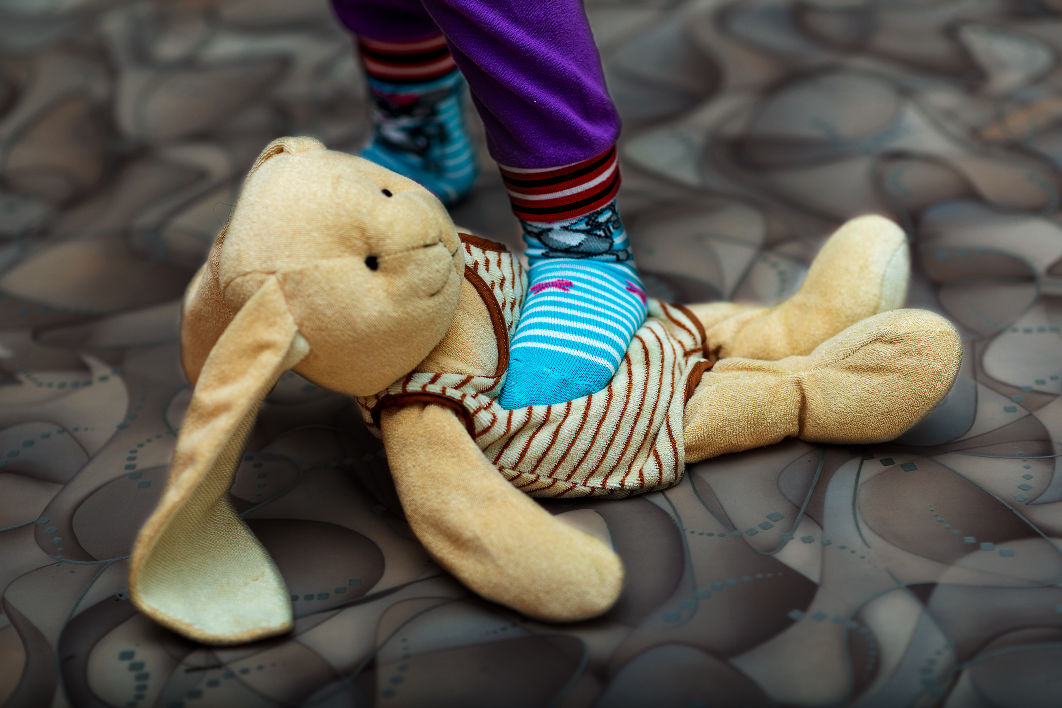 A small child stepping on a stuffed rabbit - the concept of domestic violence. Selective Focus.