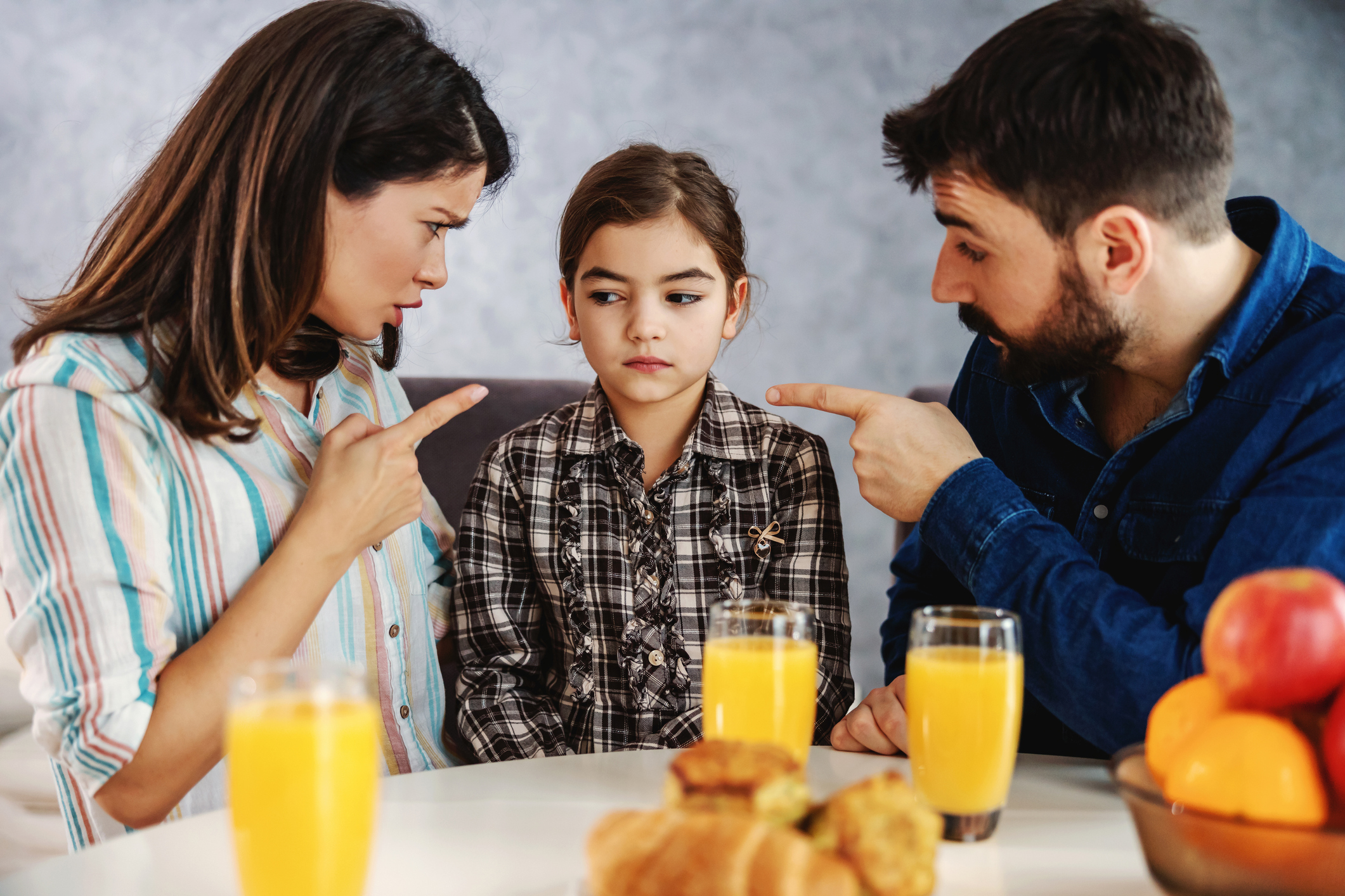 Mother and father scolding their daughter. They pointing fingers at her.