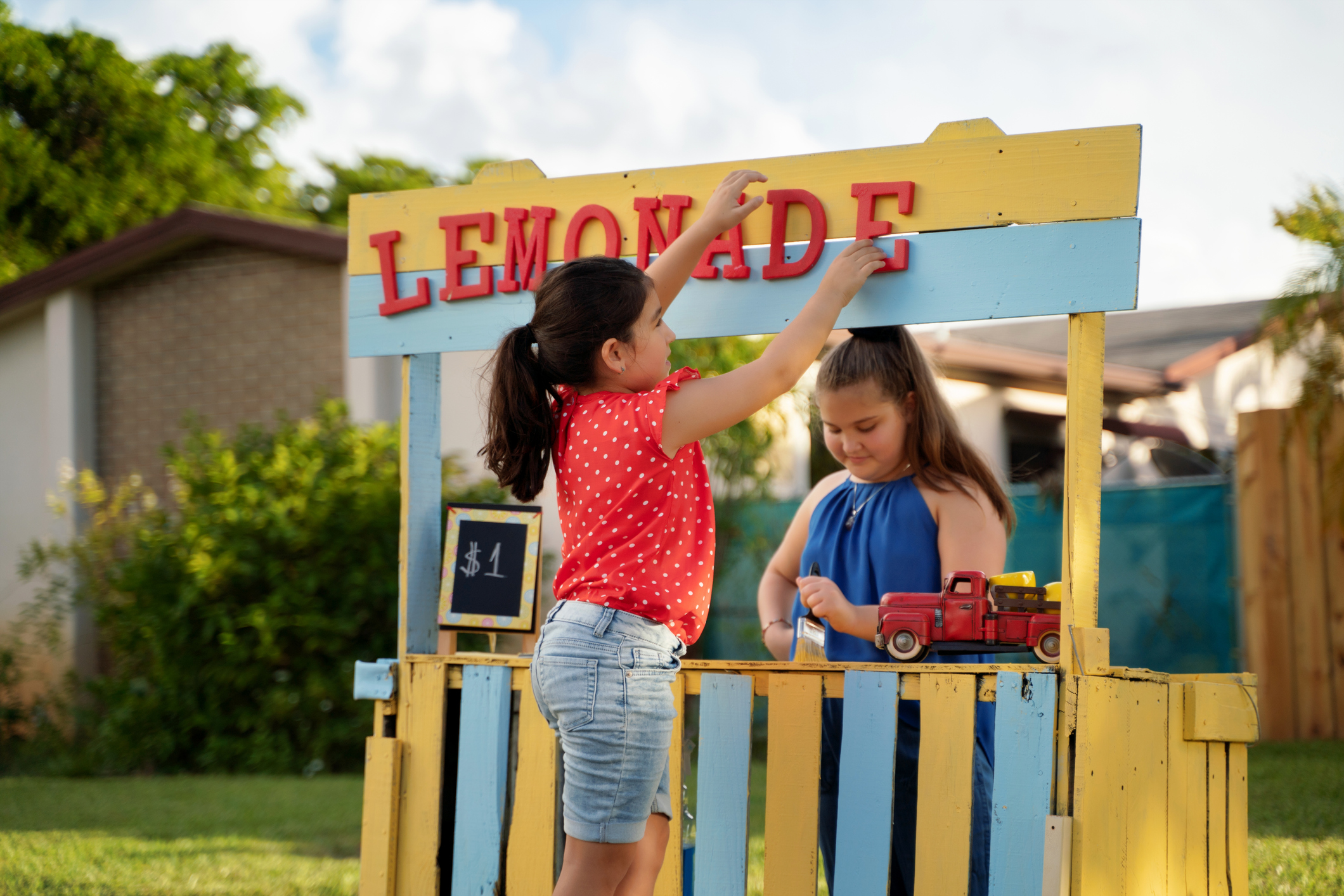 Two hispanic girls putting the last details on her soon to be open lemonade stand