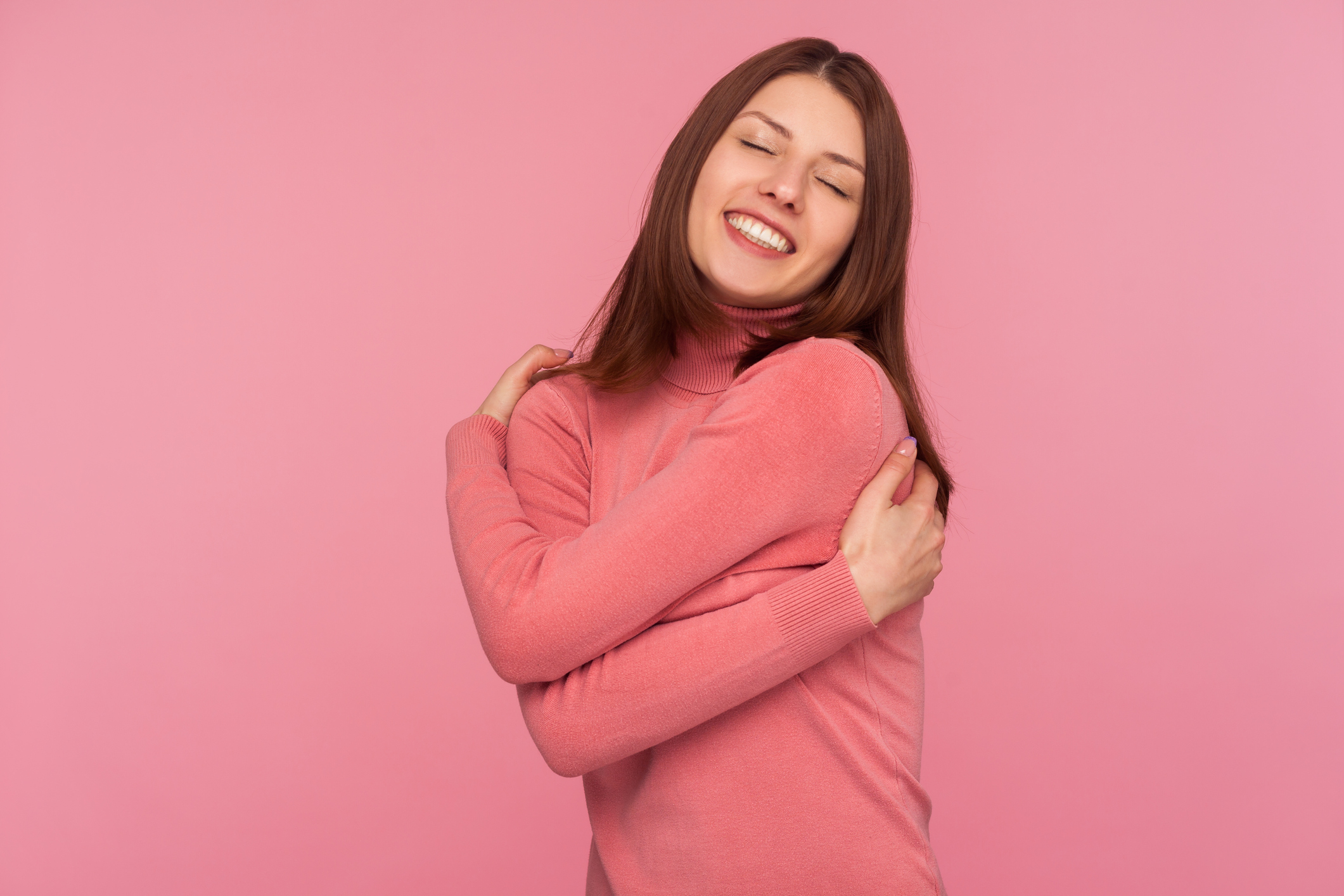 Positive narcissistic woman with brown hair tightly embracing herself standing with closed eyes, calming and supporting herself