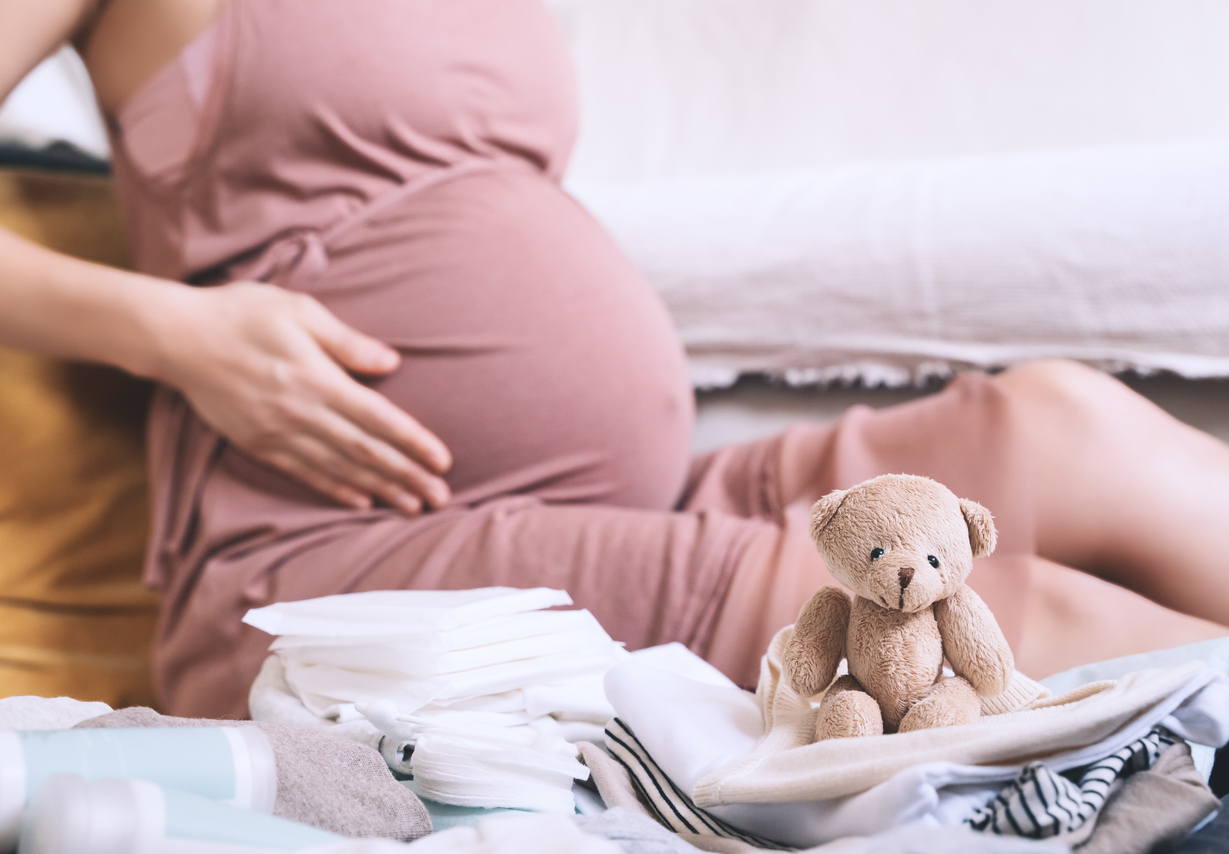 Pregnant woman hugging belly and packing maternity hospital bag. Beautiful mother during pregnancy waiting for baby preparing suitcase of clothes, toy and necessities for newborn child birth.