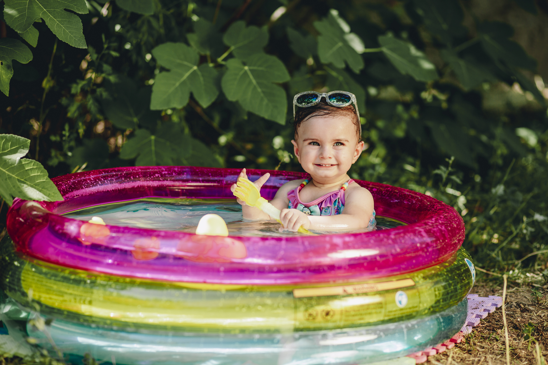 Cheerful baby enjoying her day in sumer in her pool holding plastic scoop