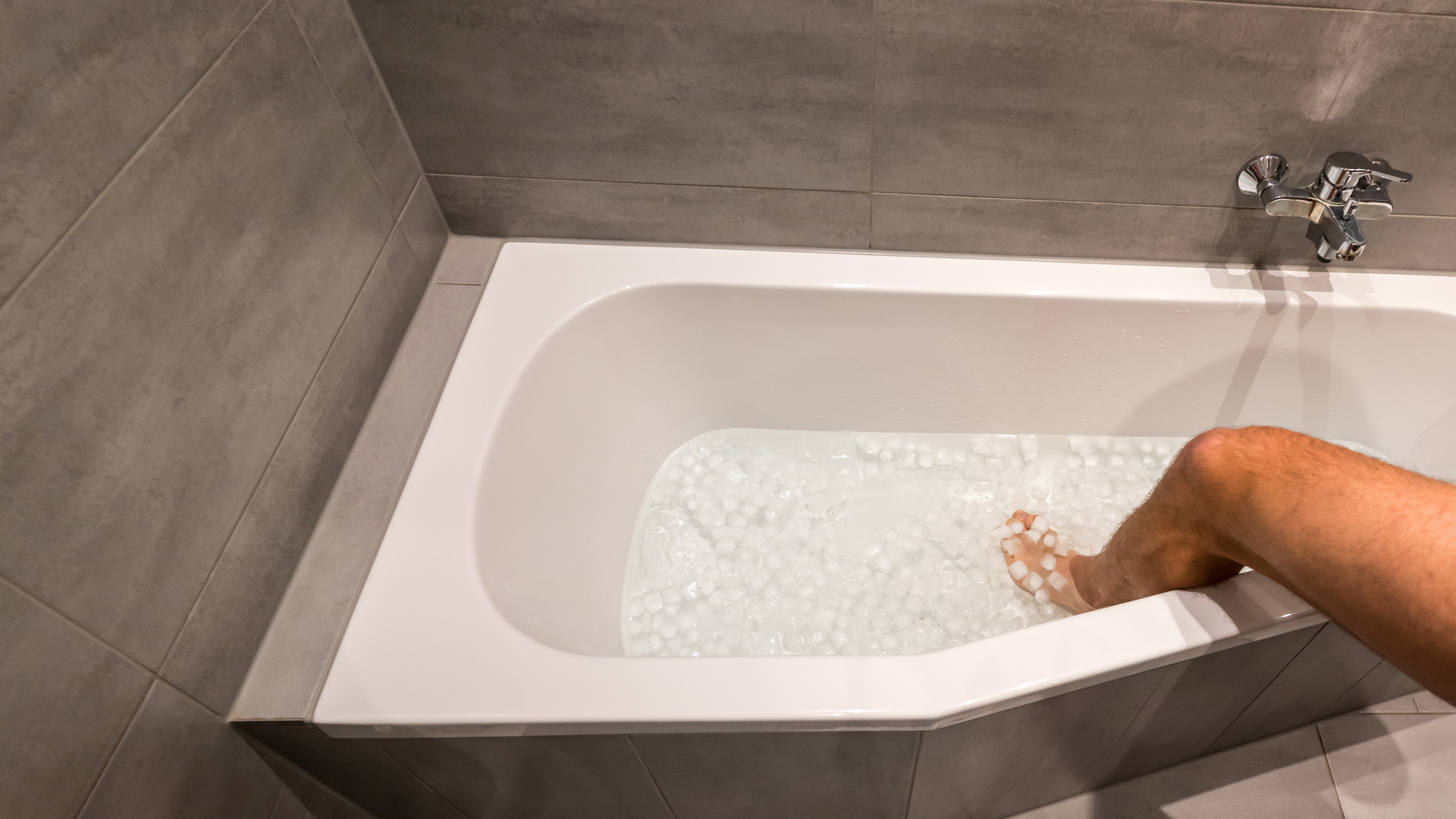 Man going into a bathtub filled with cold water and ice cubes