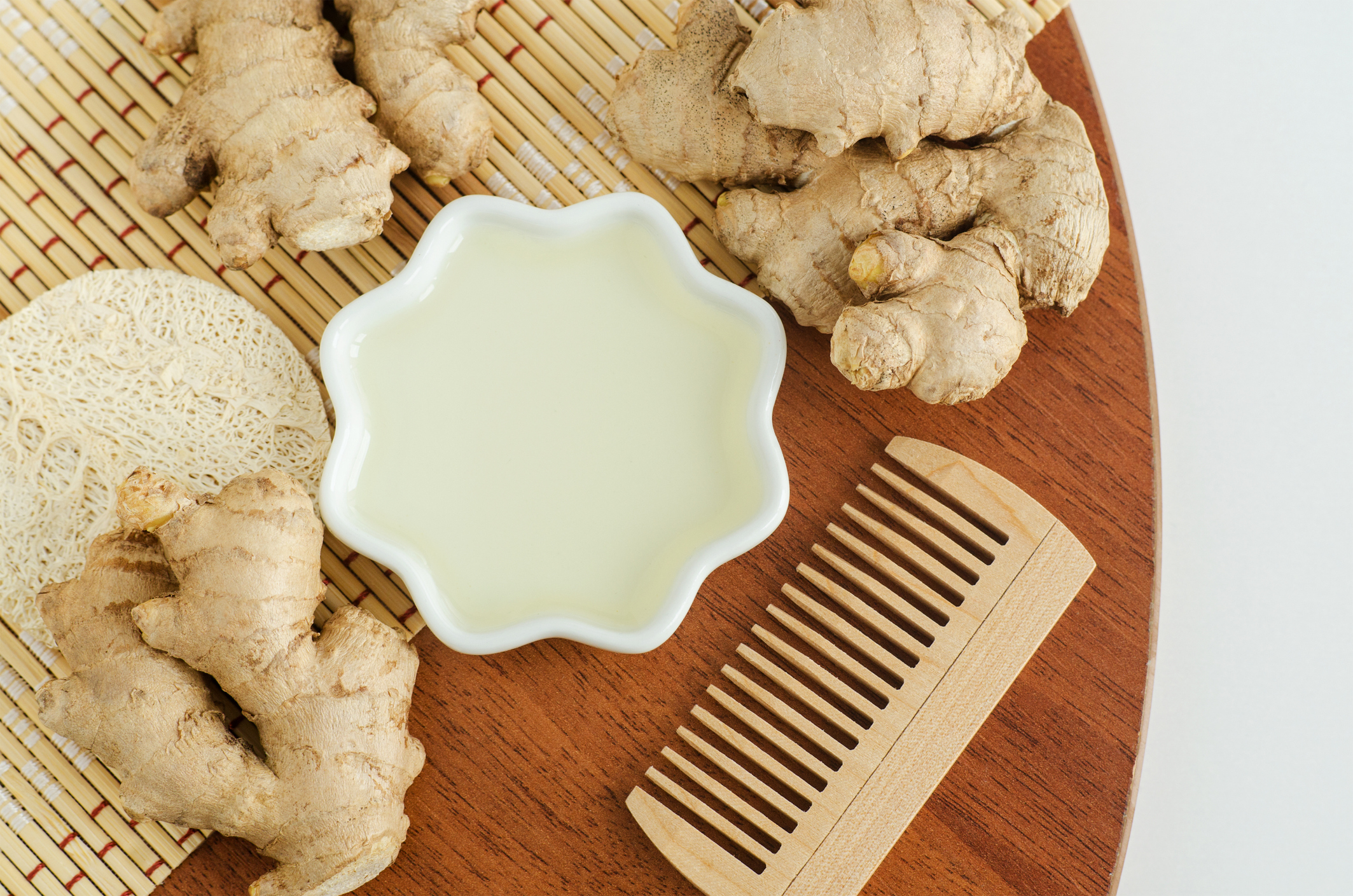 Small bowl with ginger juice (extract, tincture, infusion, perfume) and wooden hairbrush. Aromatherapy, spa and natural hair care. Flat lay, copy space