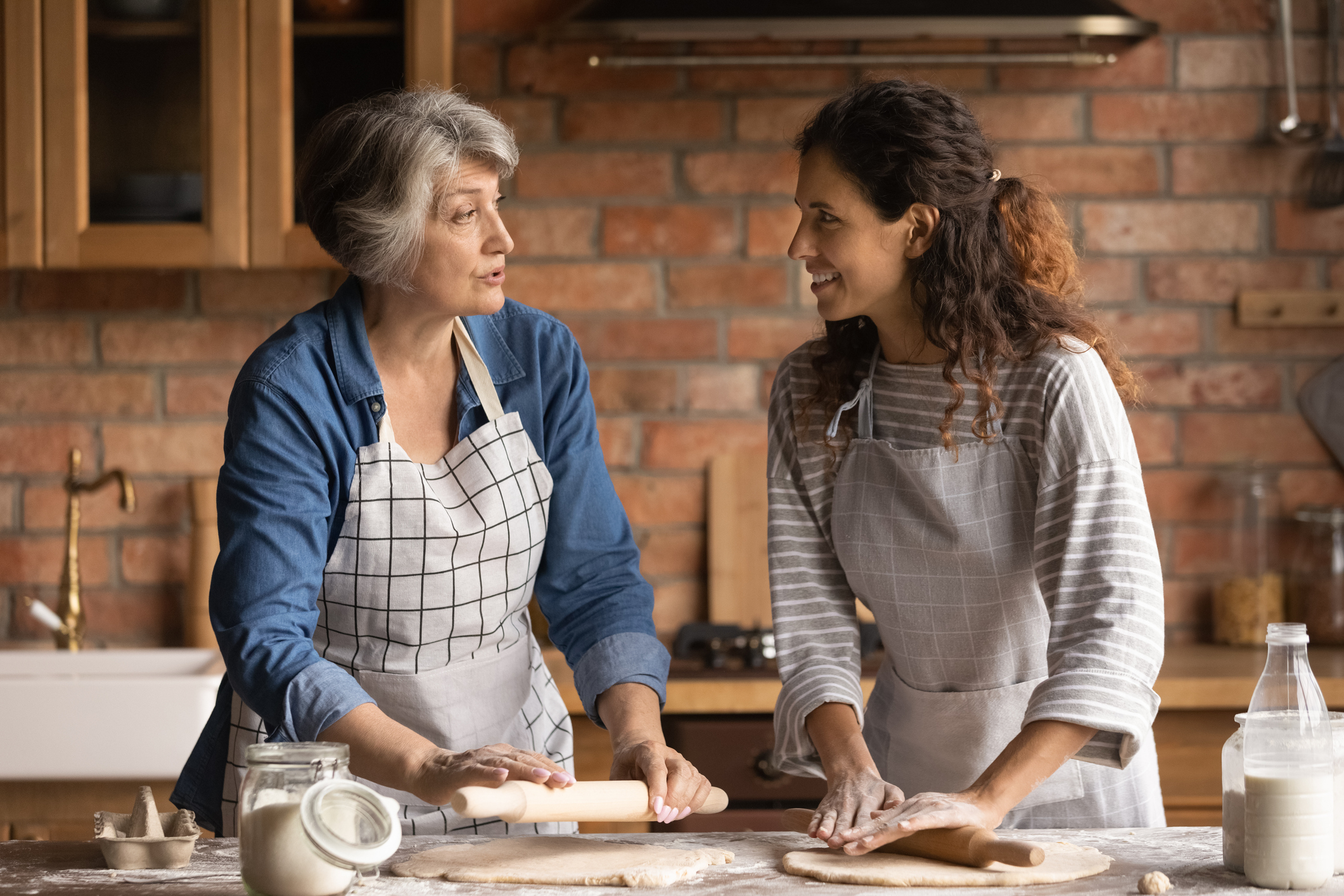 Mature woman with grownup daughter chatting, cooking homemade pastry