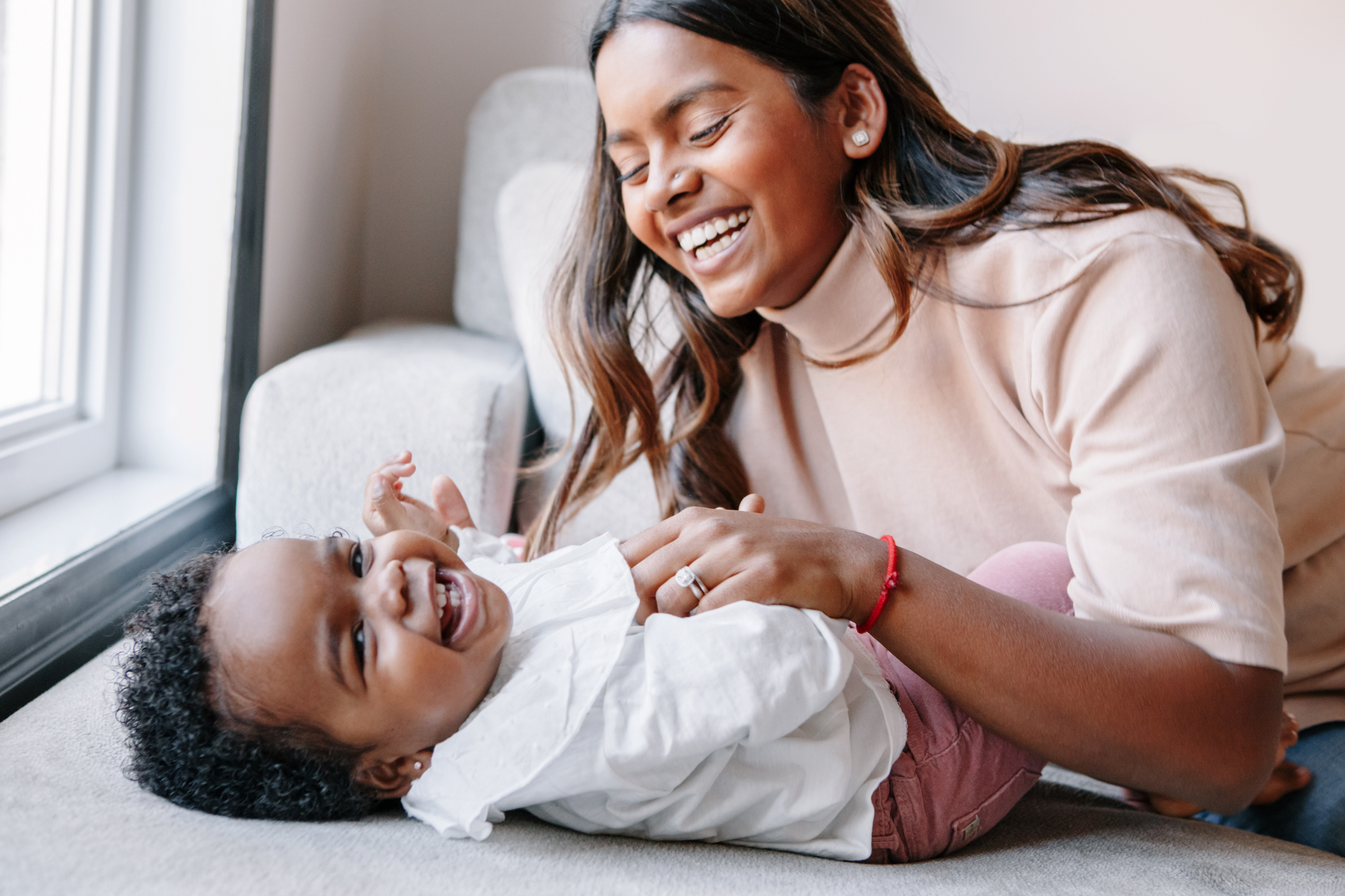 Happy smiling laughing Indian mother playing with black baby girl daughter. Family mixed race people mom and a kid together hugging at home. Authentic candid lifestyle with infant kid child.