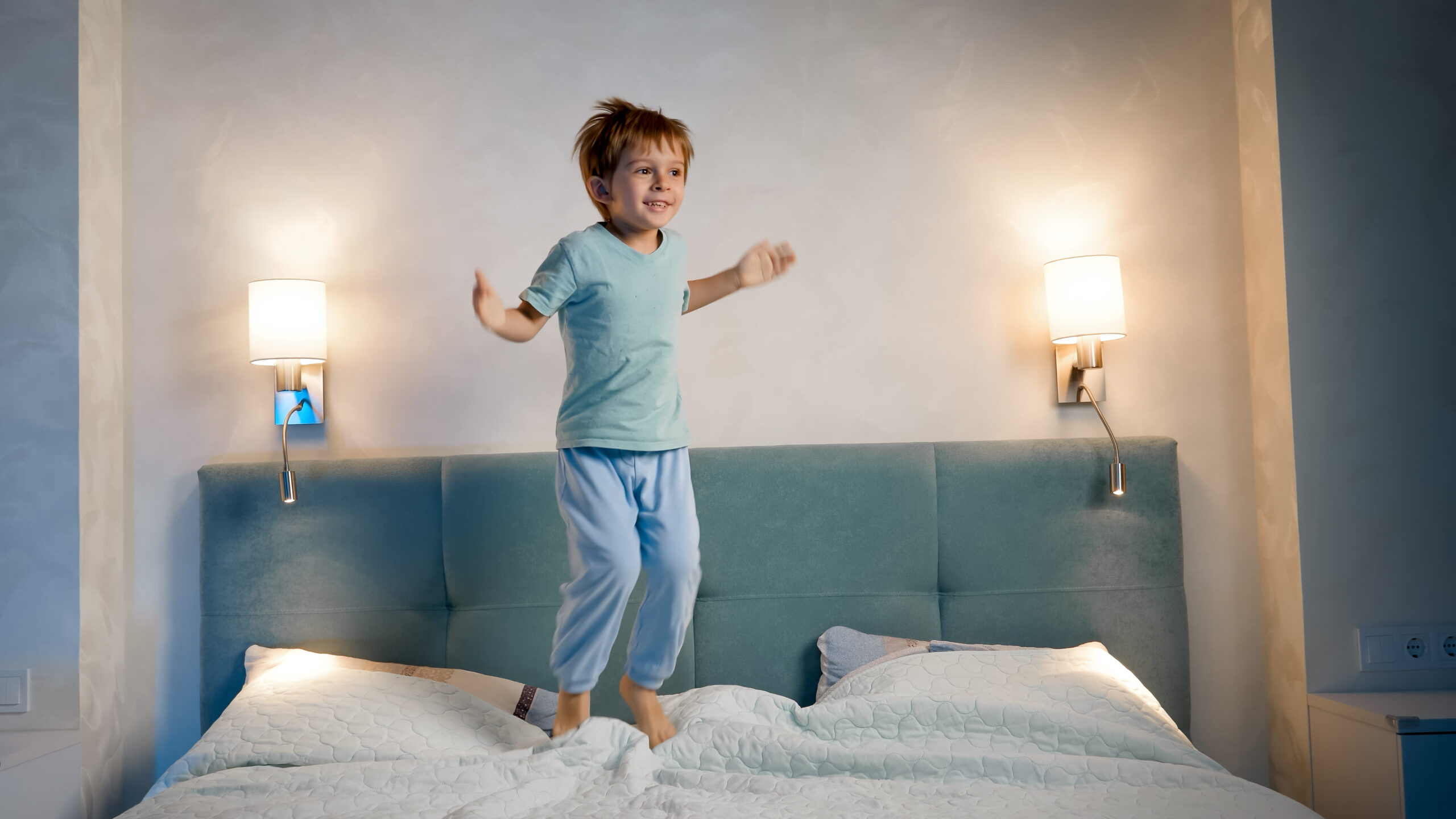 Happy laughing and smiling toddler boy in pajamas skipping and jumping up high on parent's bed at night before going to sleep