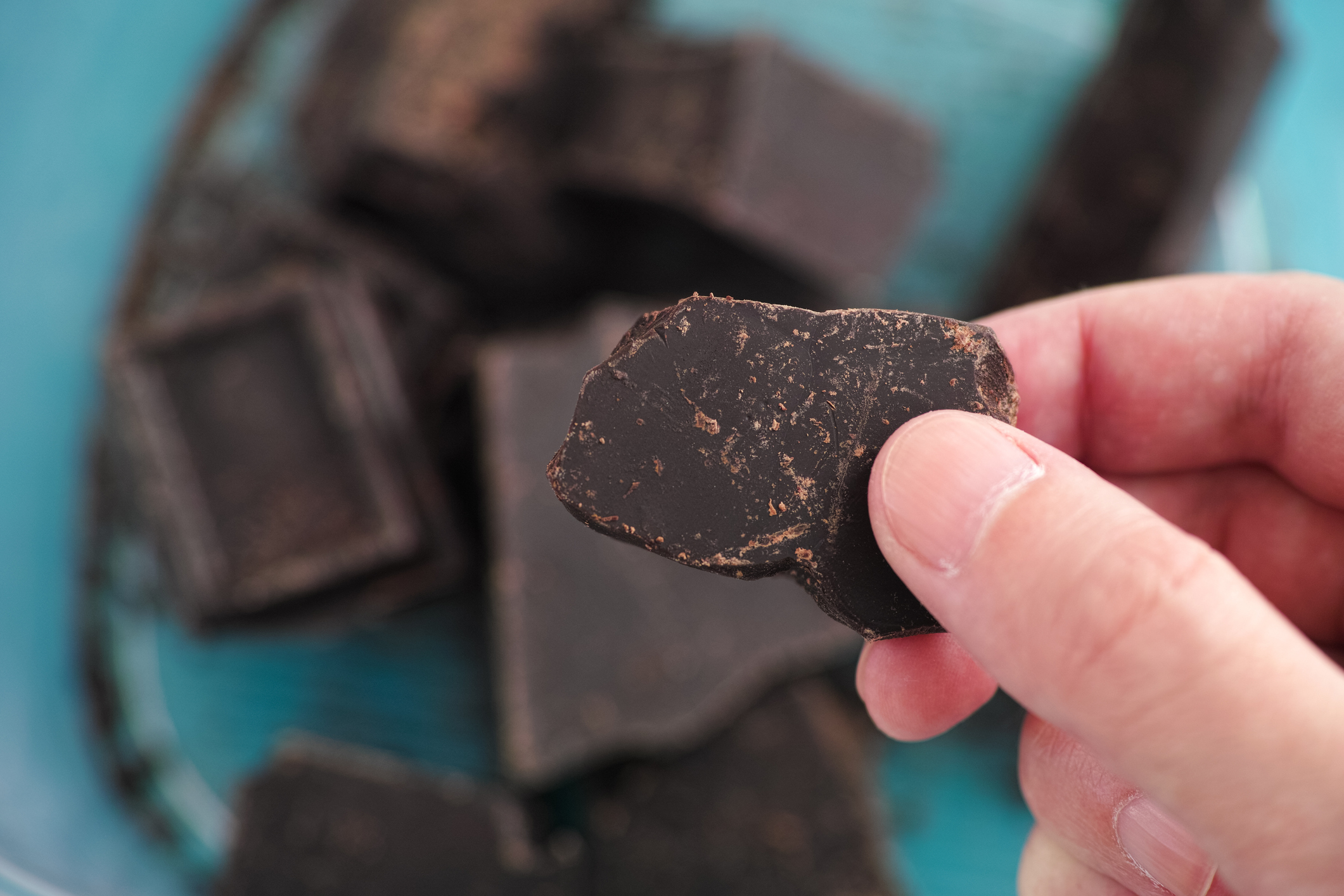 A man holding a piece of homemade broken dark chocolate in his hand