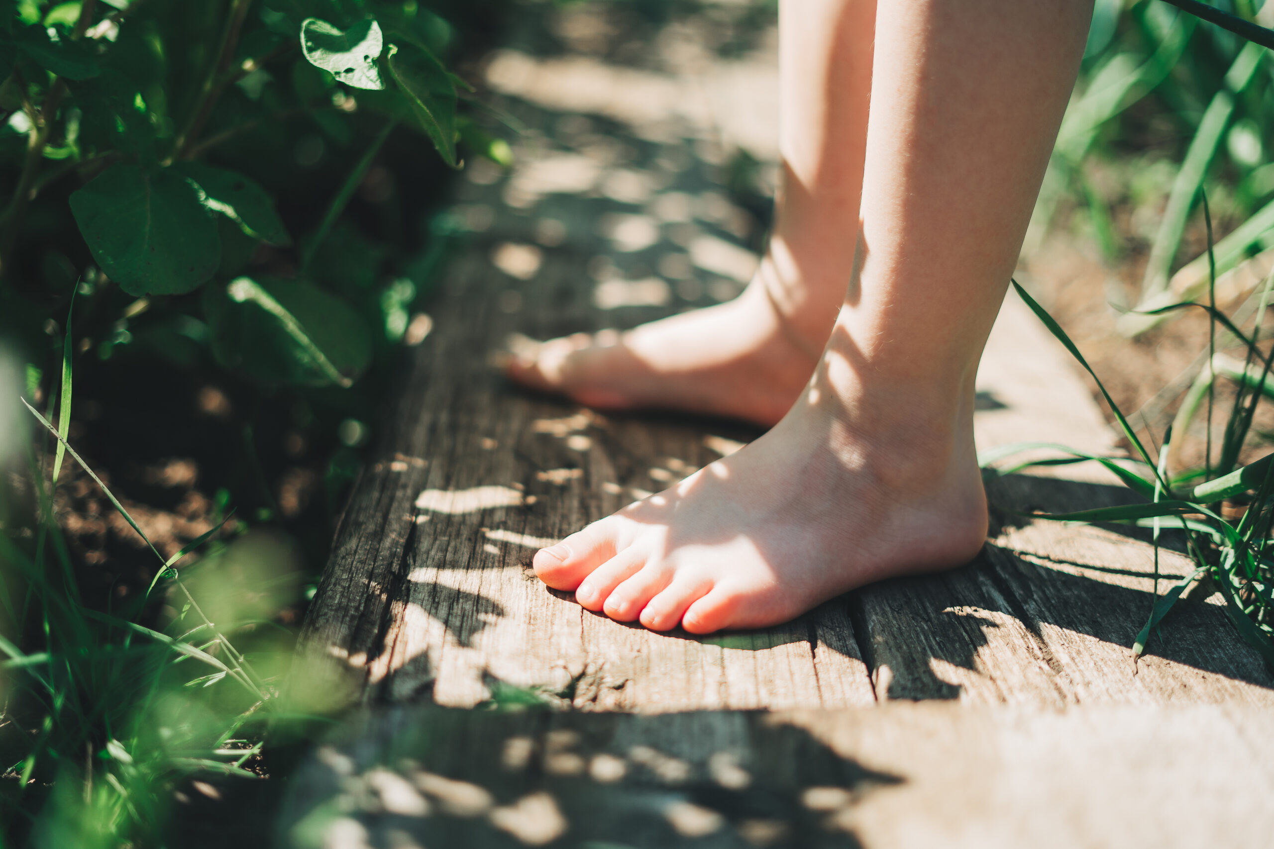 Kid walking barefoot on wood plank at a grass field
