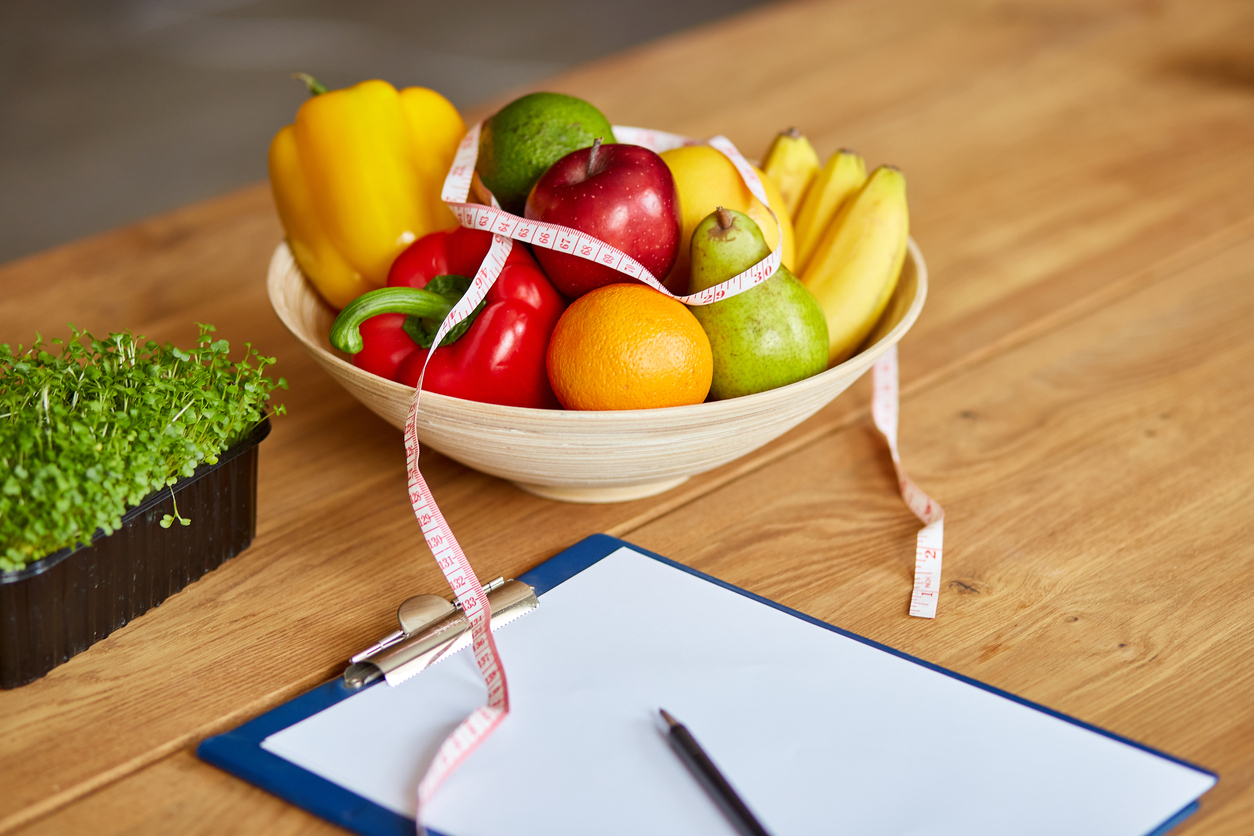 Top view of Nutritionist, dietitian workplace with measuring tape and bowl with healthy vegetables and fruits