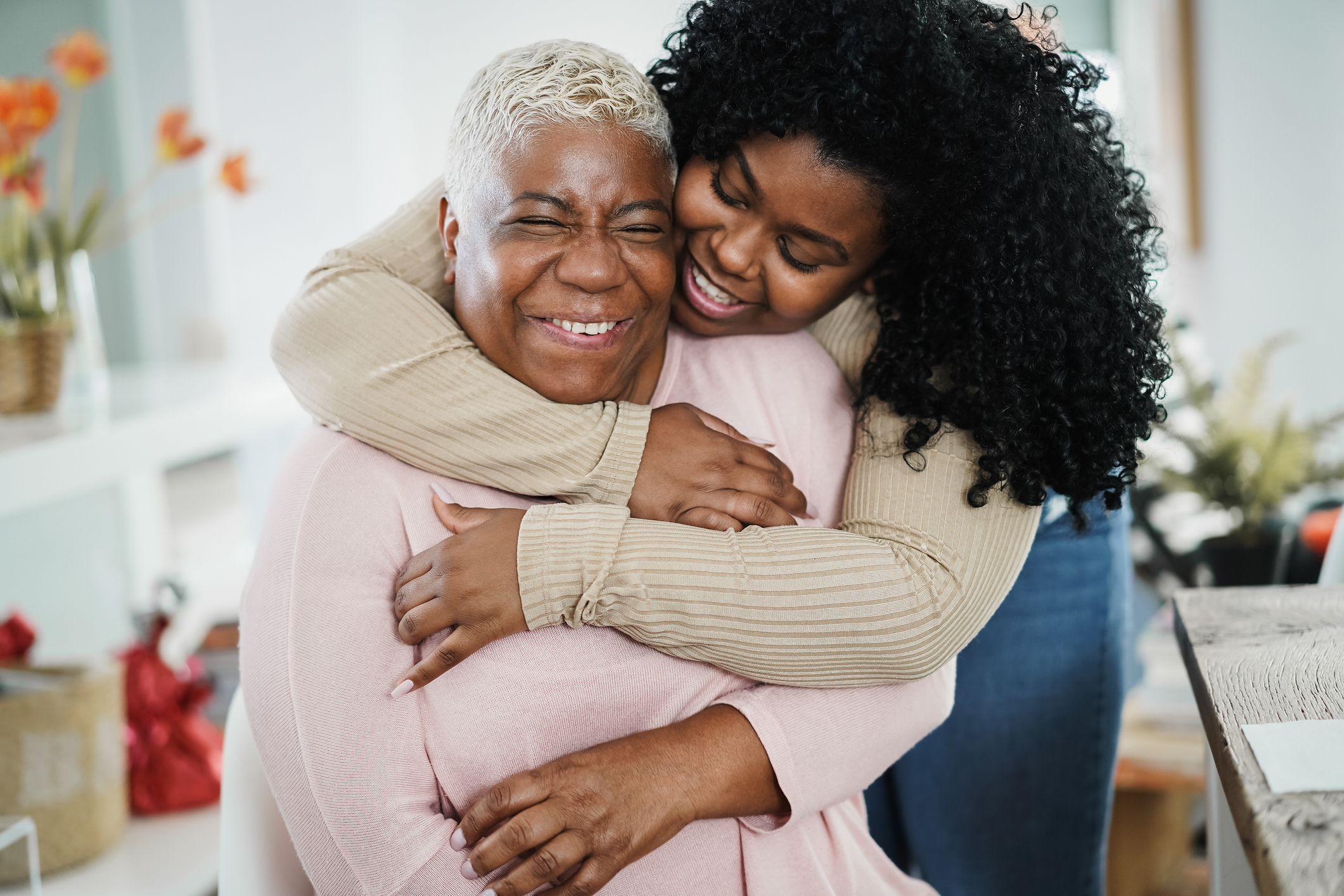 African daughter hugging her mum indoors at home - Main focus on senior woman face