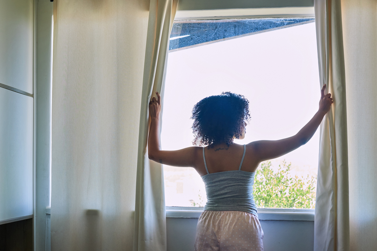 Rearview shot of a woman standing by her bedroom window while wearing pyjamas