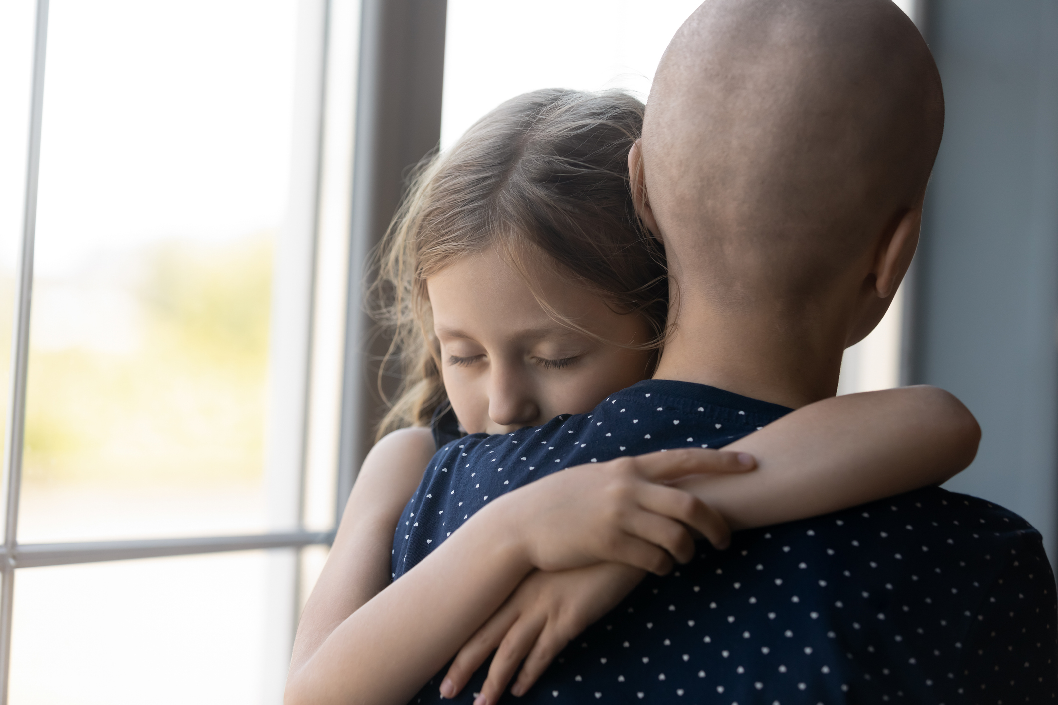 Sad serious daughter girl hugging hairless mom with cancer