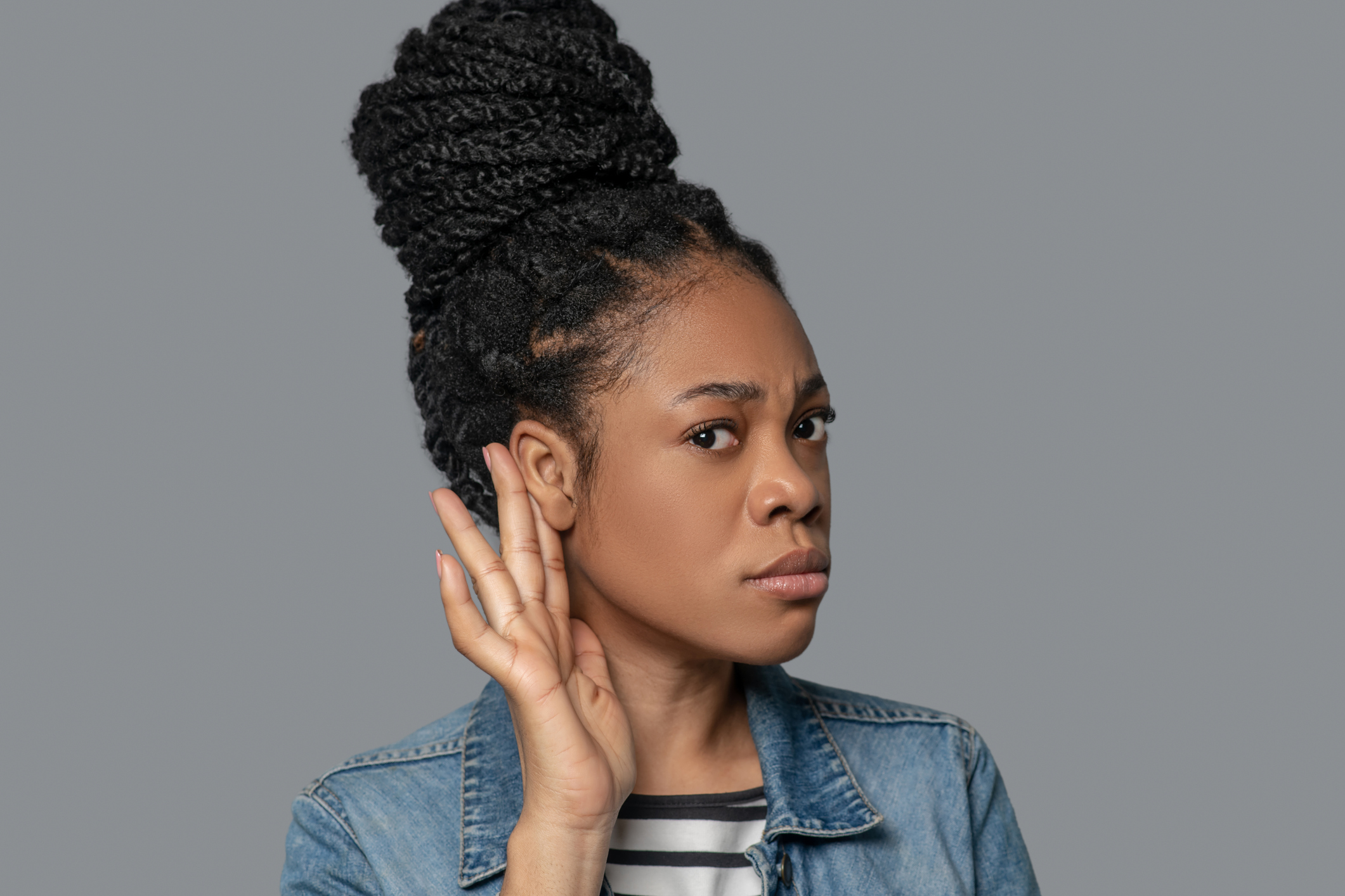 Picture of a dark-skinned young woman touching her ear in listening gesture