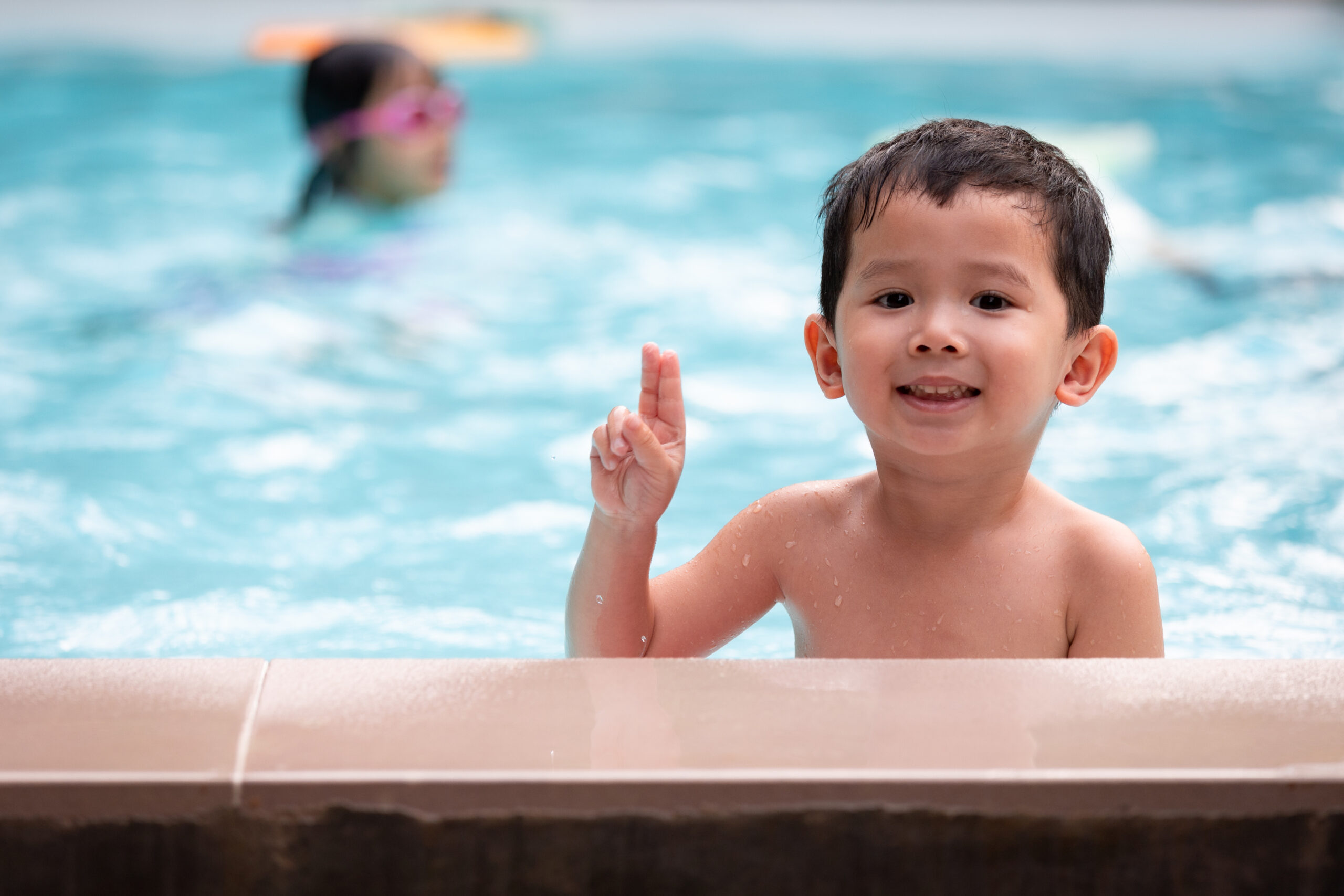 Portrait of asian little boy looking at camera and smiling while playing water in the swimming pool.