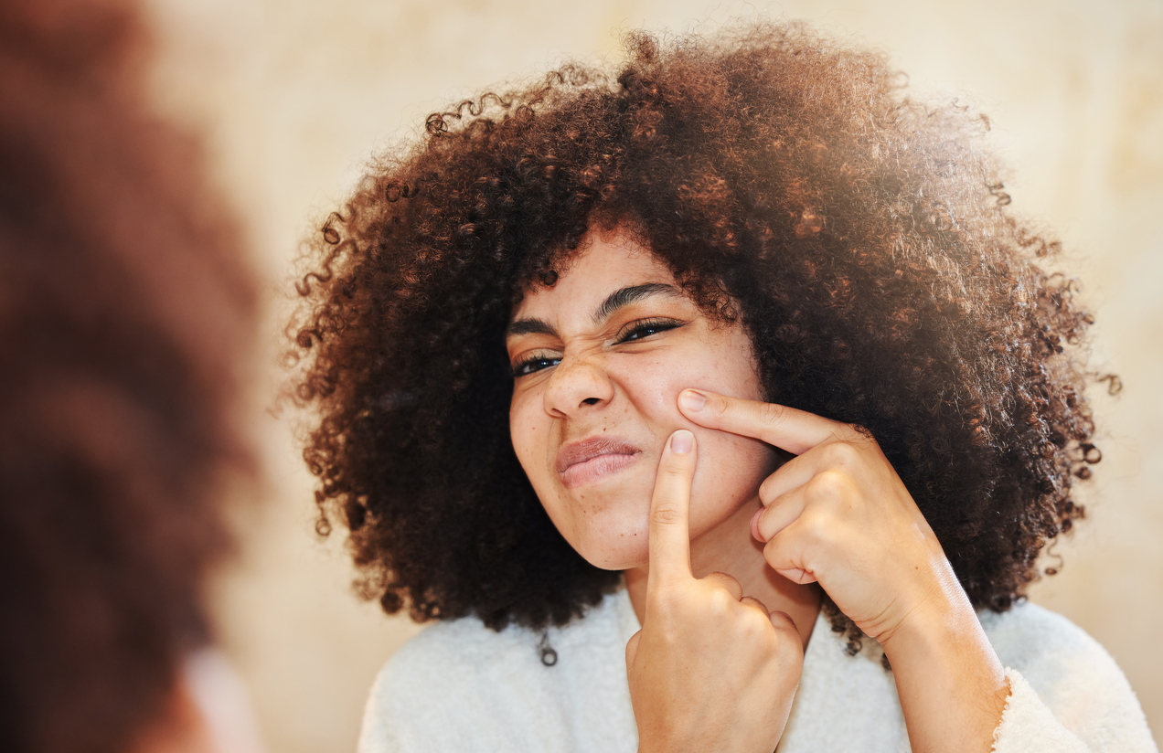 Shot of a young woman squeezing a pimple while looking in the bathroom mirror