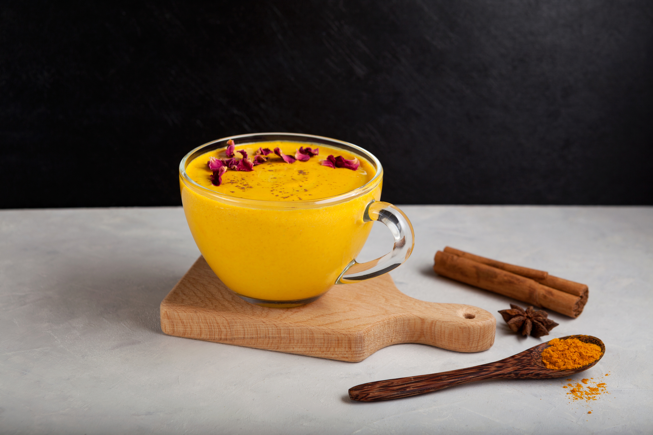 Healthy ayurvedic drink golden almond milk or Turmeric latte with curcuma powder. Trendy Asian natural detox drink with spices. Dark background, selective focus, copy space