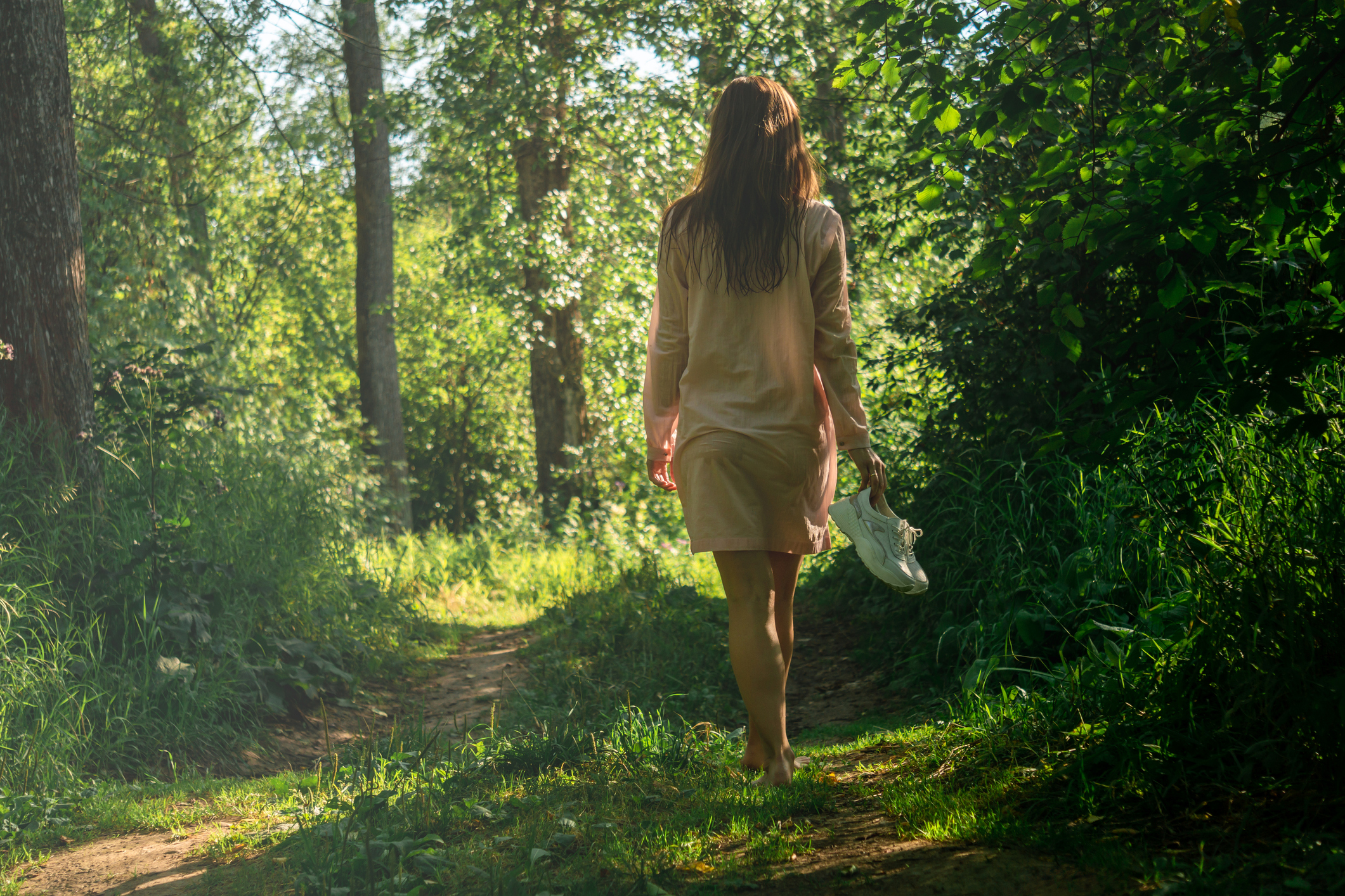 young woman walking barefoot on a forest road after bathing