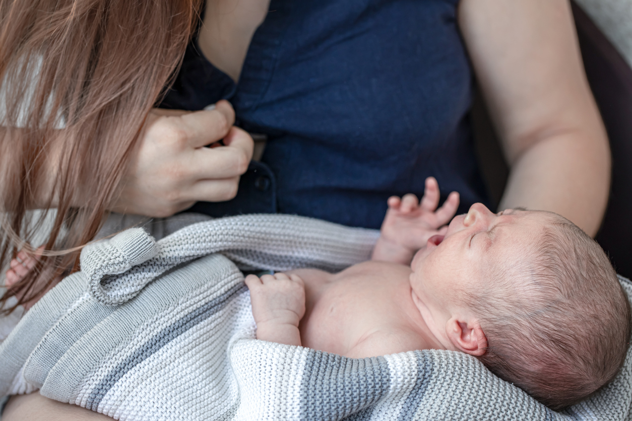 The newborn baby is crying, the young mother is breastfeeding the baby.