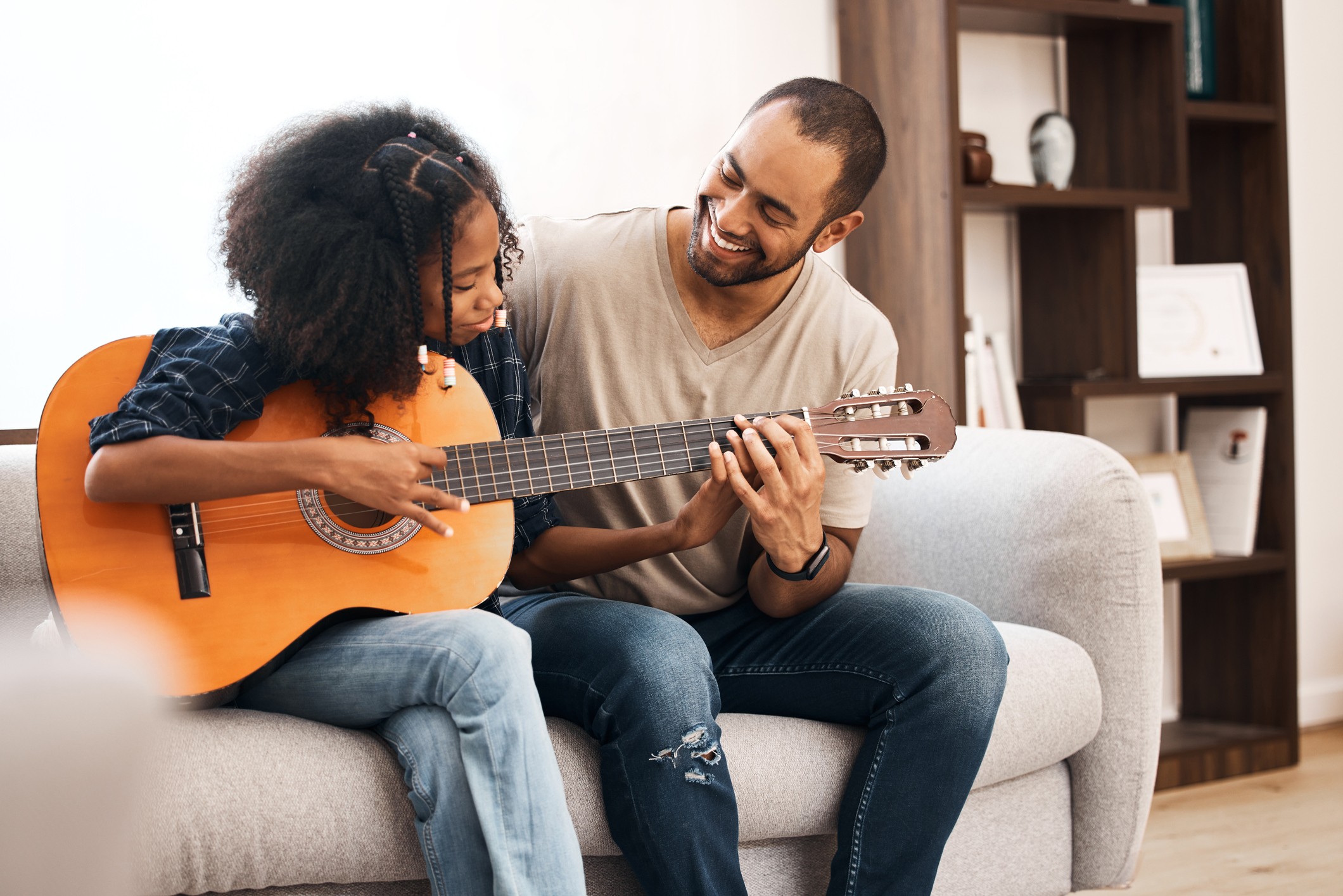 Shot of a young girl learning to play the guitar with her father at home