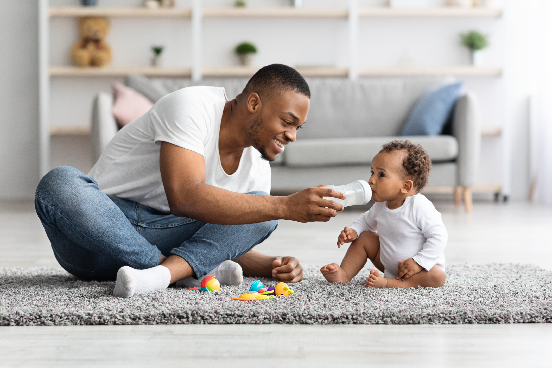 Caring young black dad giving water to his little baby at home