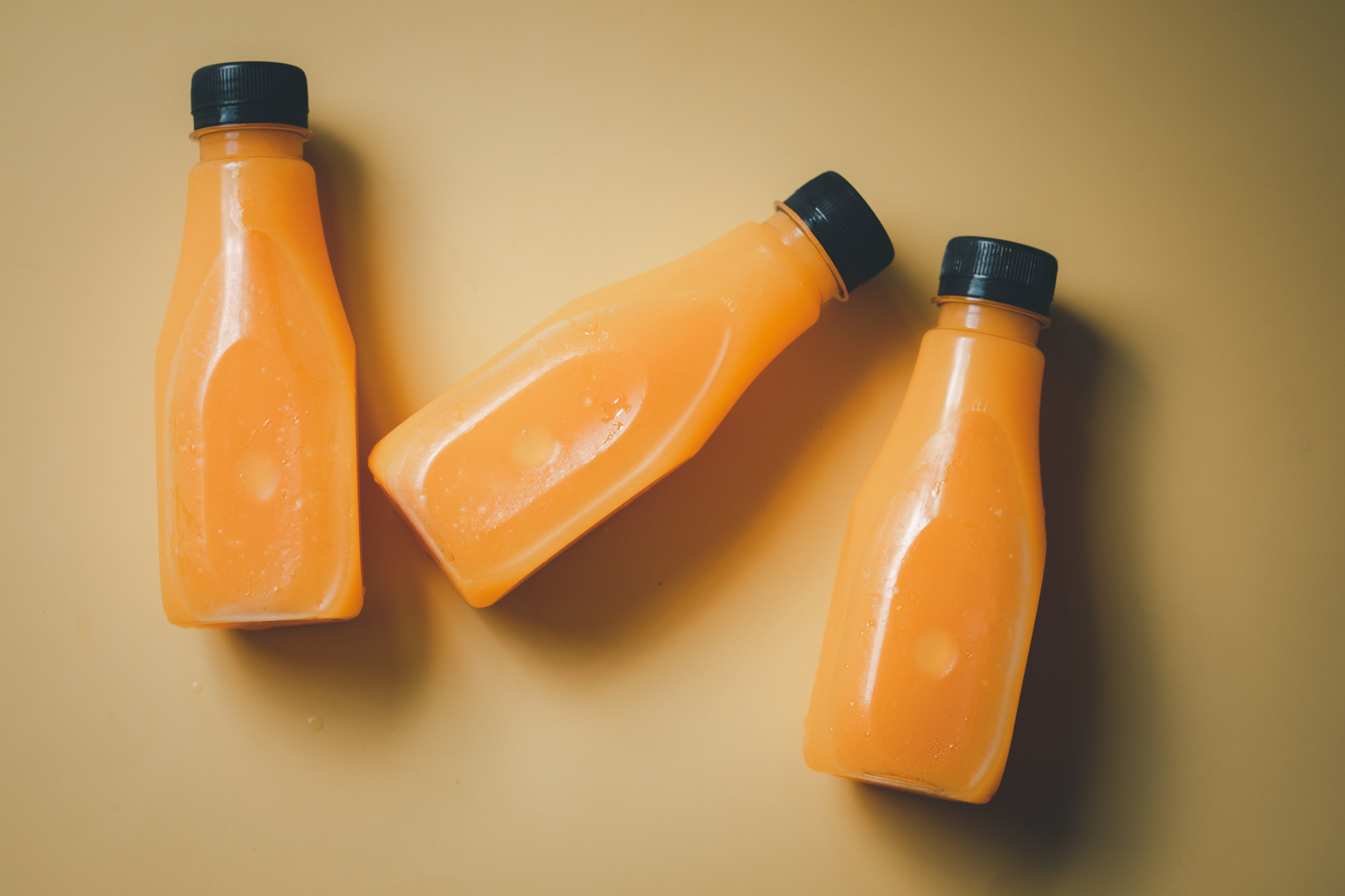 Three orange juices in plastic bottle on a yellow background. Summer refreshing