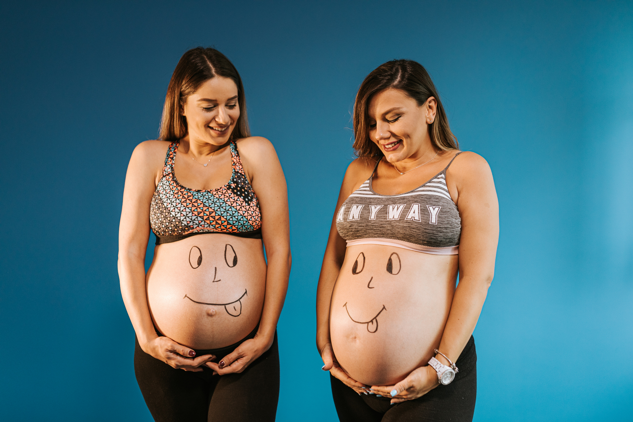 Two pregnant female friends with smiley face drawing on their pregnant bellies having fun and posing