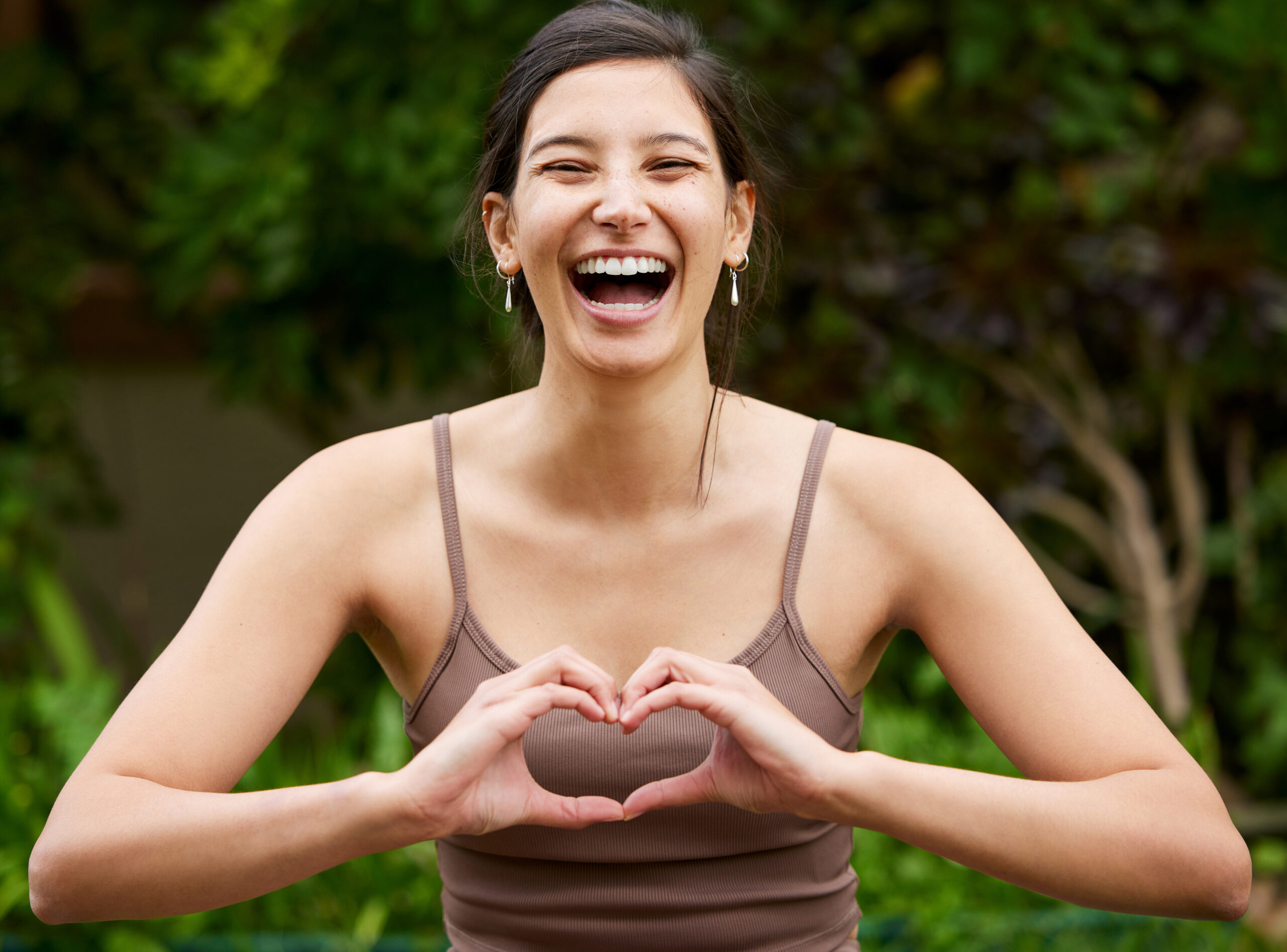 Portrait of a young woman making a heart shape with her hands while exercising outdoors