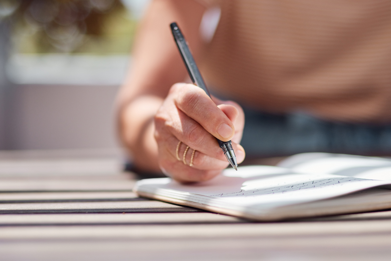 Shot of an unrecognisable woman writing in a notebook on the balcony at home