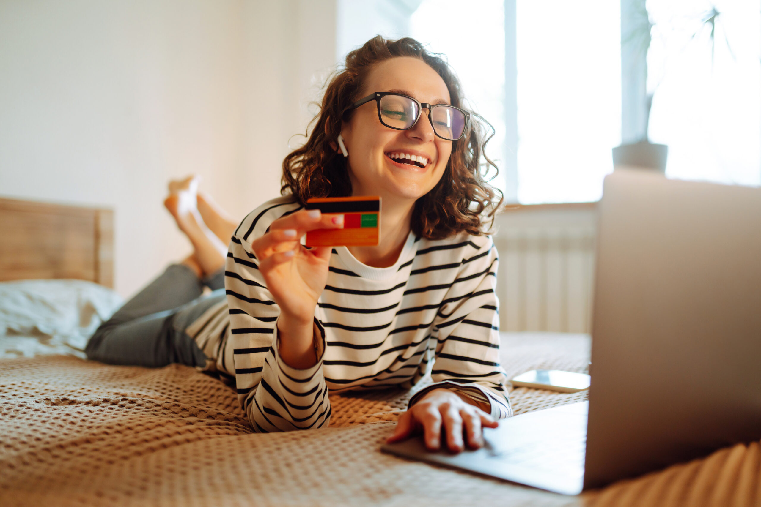 Online shopping аt home. A young woman holds a credit card and uses a laptop.