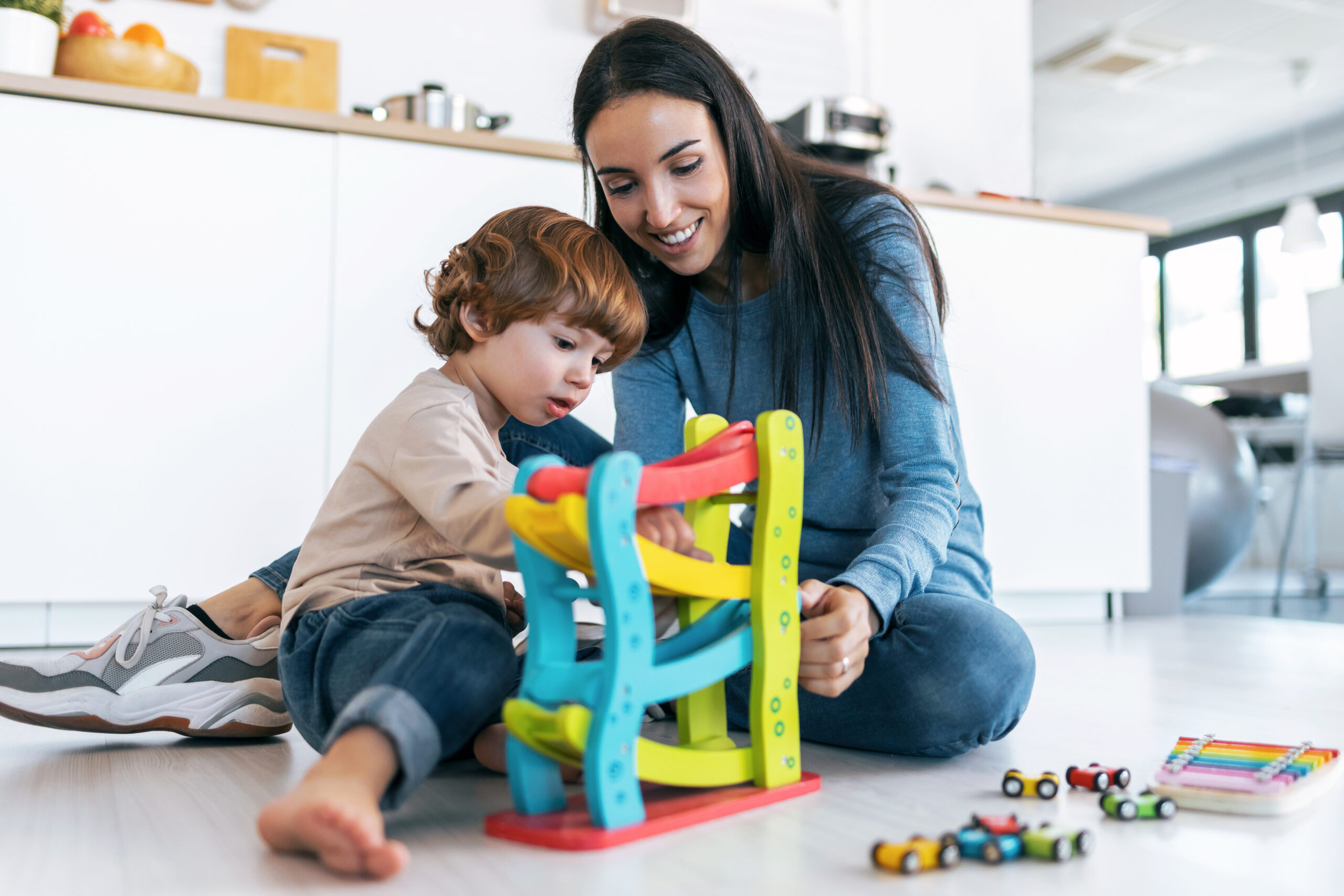 Young beautiful mother playing on the floor with her son in living room at home.