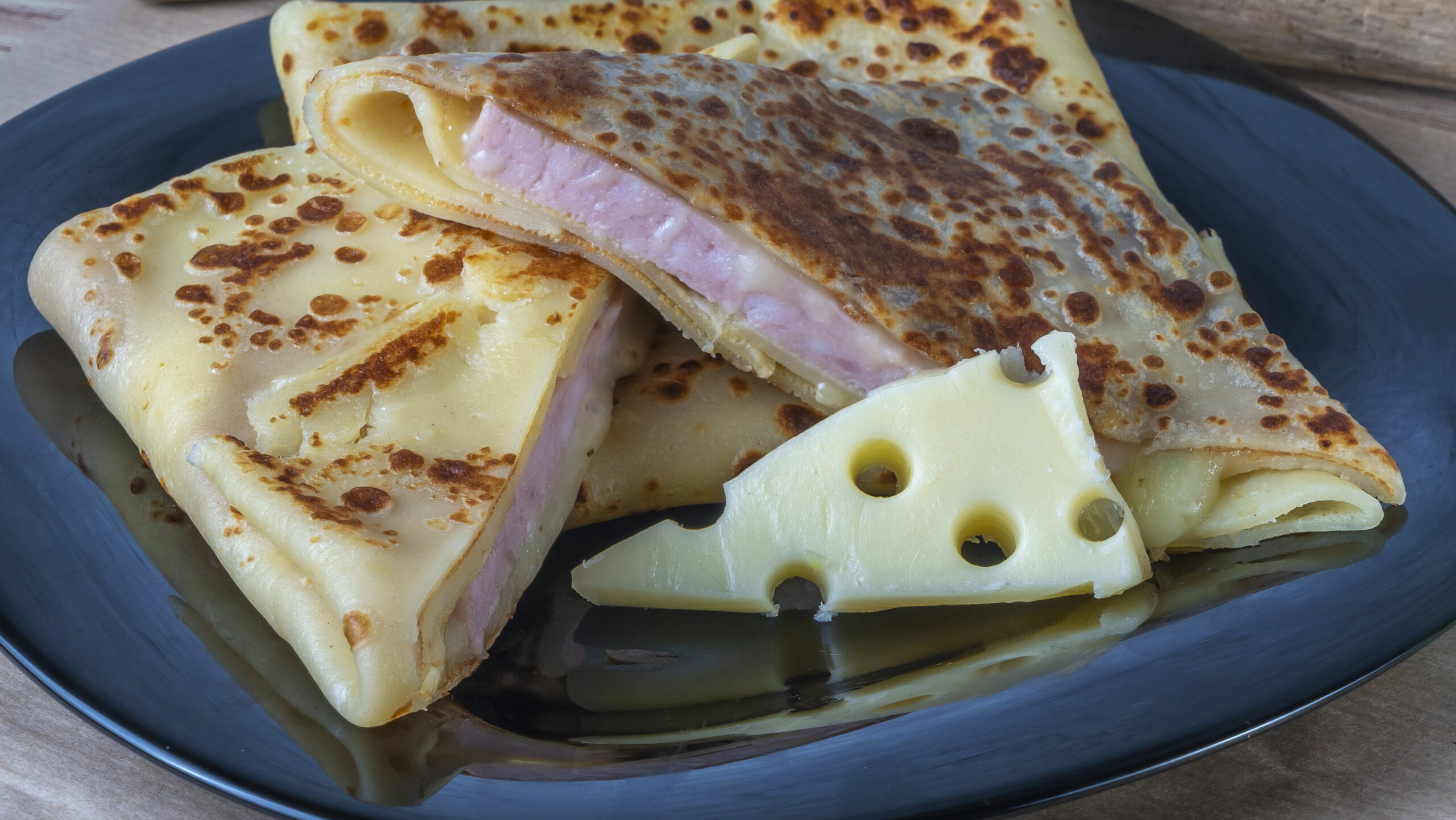 Crepe stuffed with cheese and ham. Pancake with cheese and ham on a black plate.