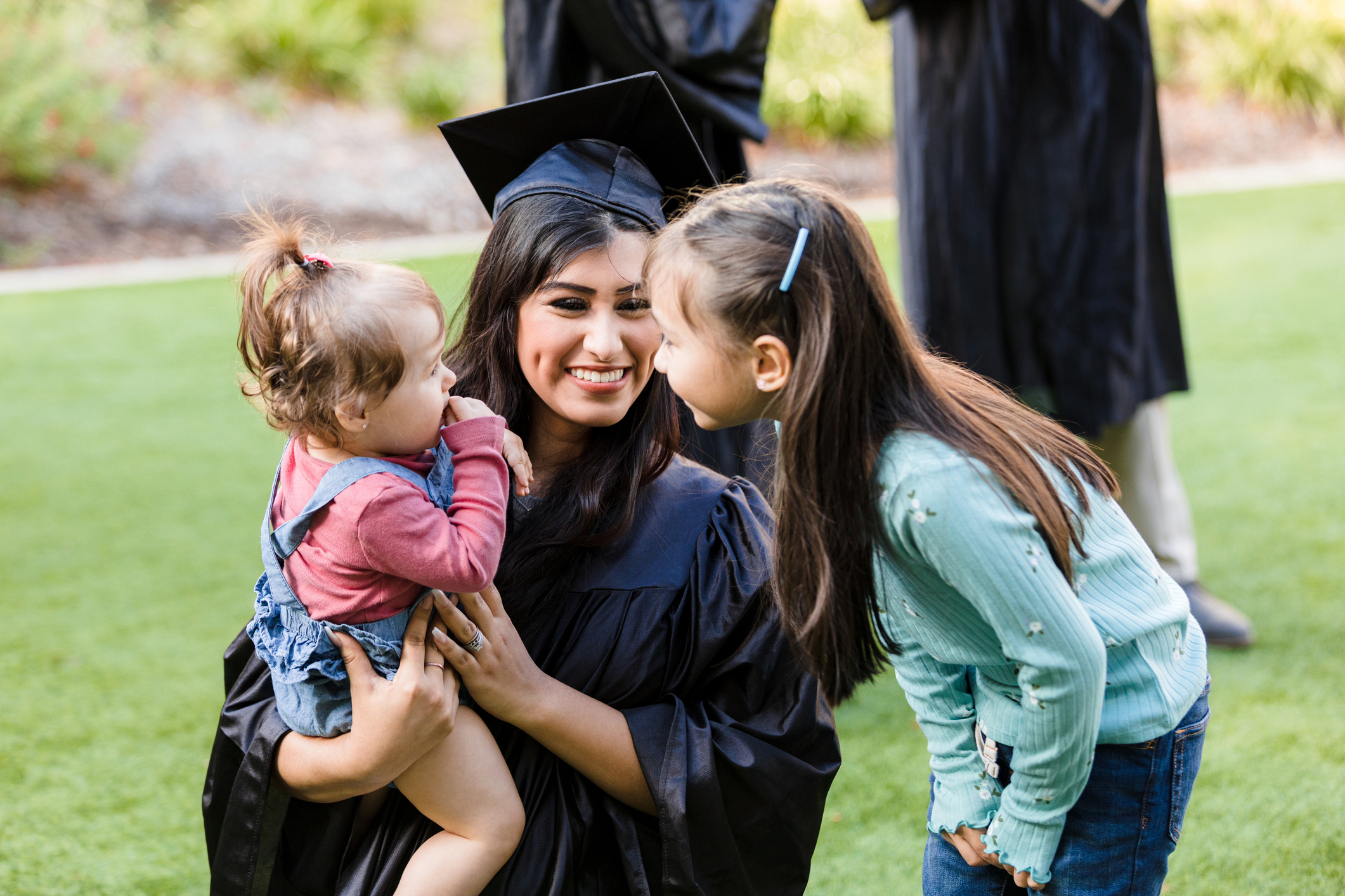 Elementary age sister talks to baby held by graduate