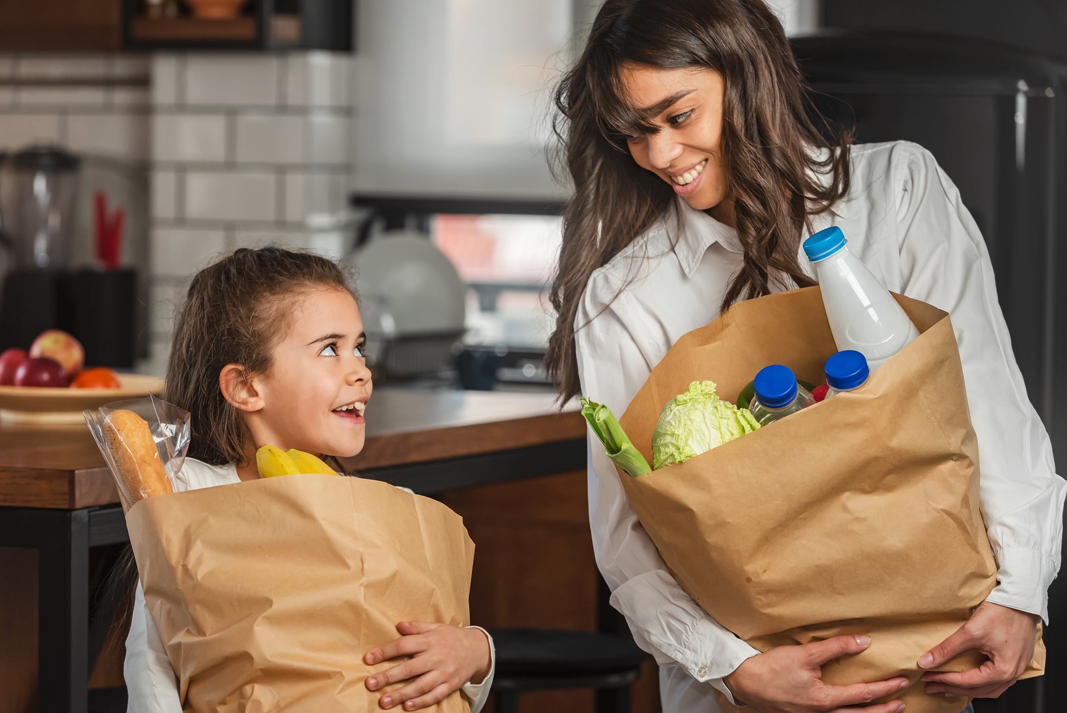 Cheerful little daughter helping the mother to carry groceries from the market