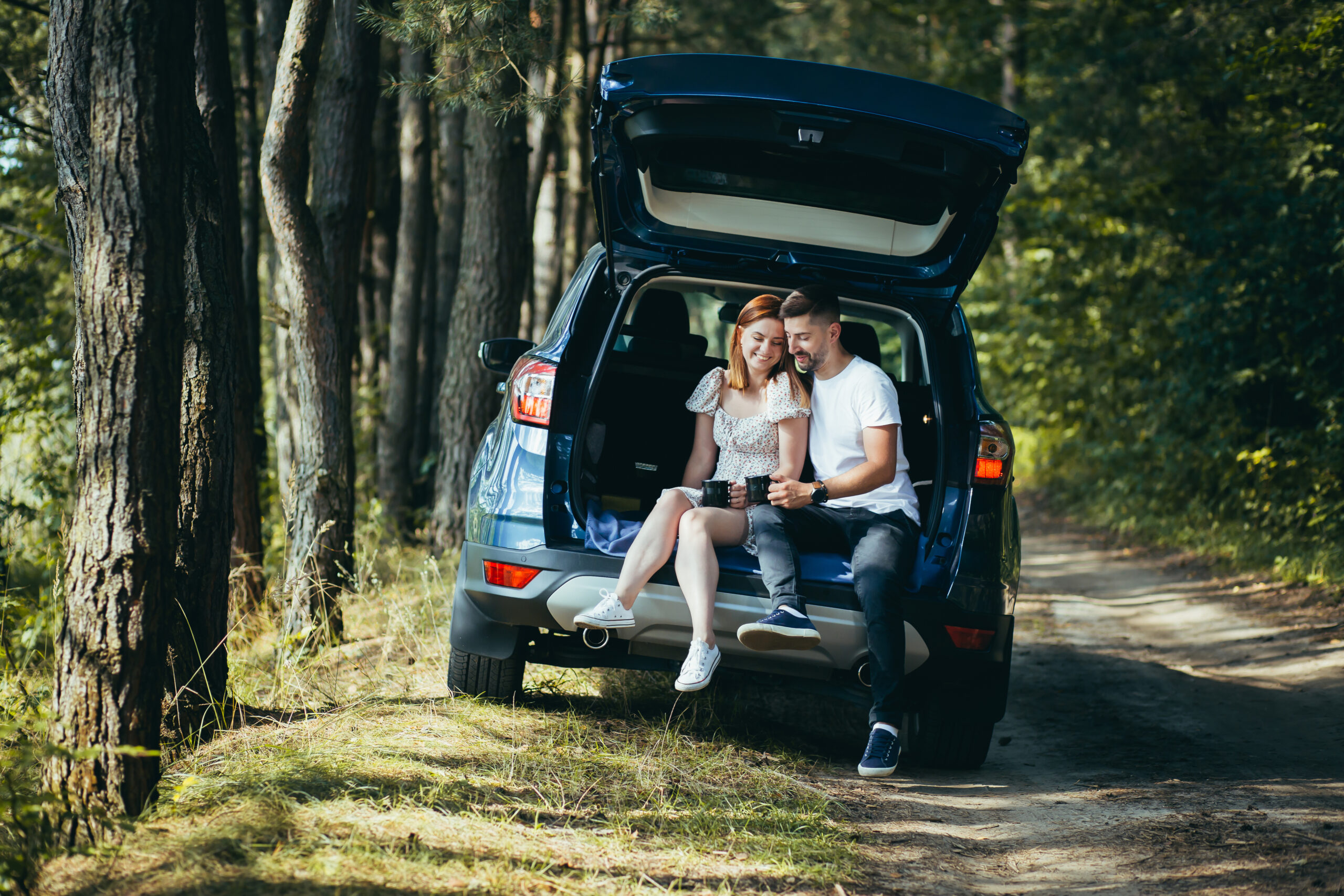 Young couple, man and woman, hugging together on a picnic, sitting in the trunk of a car in the woods, happy together