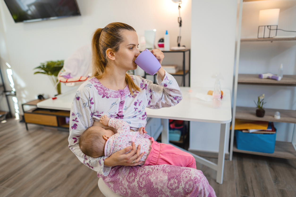 Mother drinking coffee while breastfeeding her newborn baby